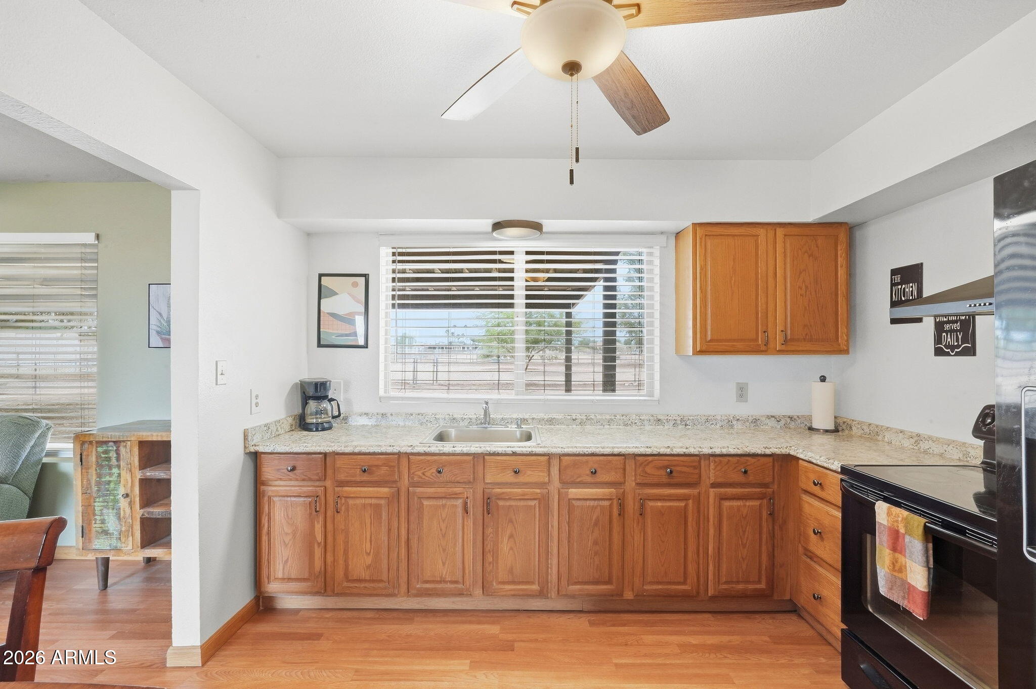 Kitchen with warm wood cabinets and a sink beneath a wide window, opening to a living area.