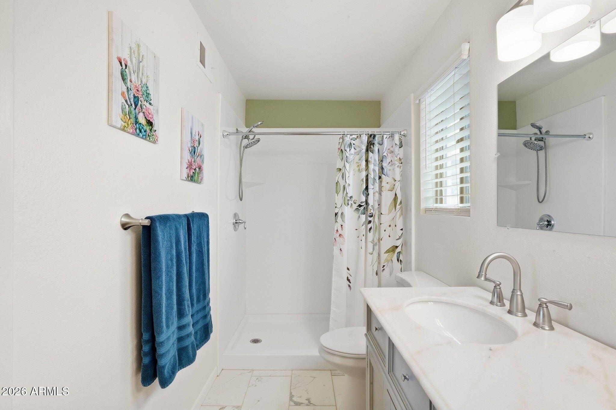 Bathroom with walk-in shower, floral curtain, white vanity, and blue towels.