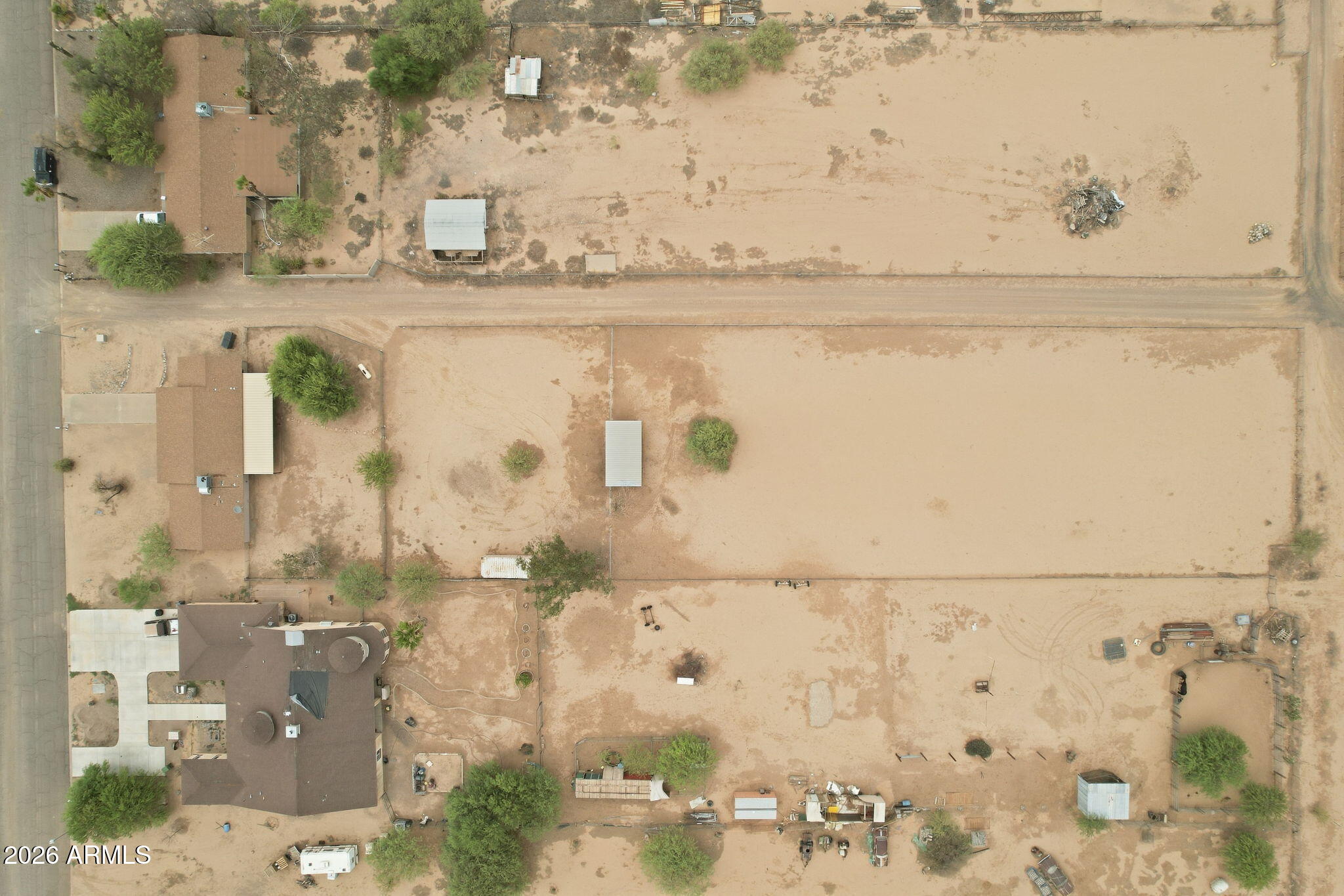 Aerial view of a desert property with two homes, fenced sandy lots, and outbuildings.