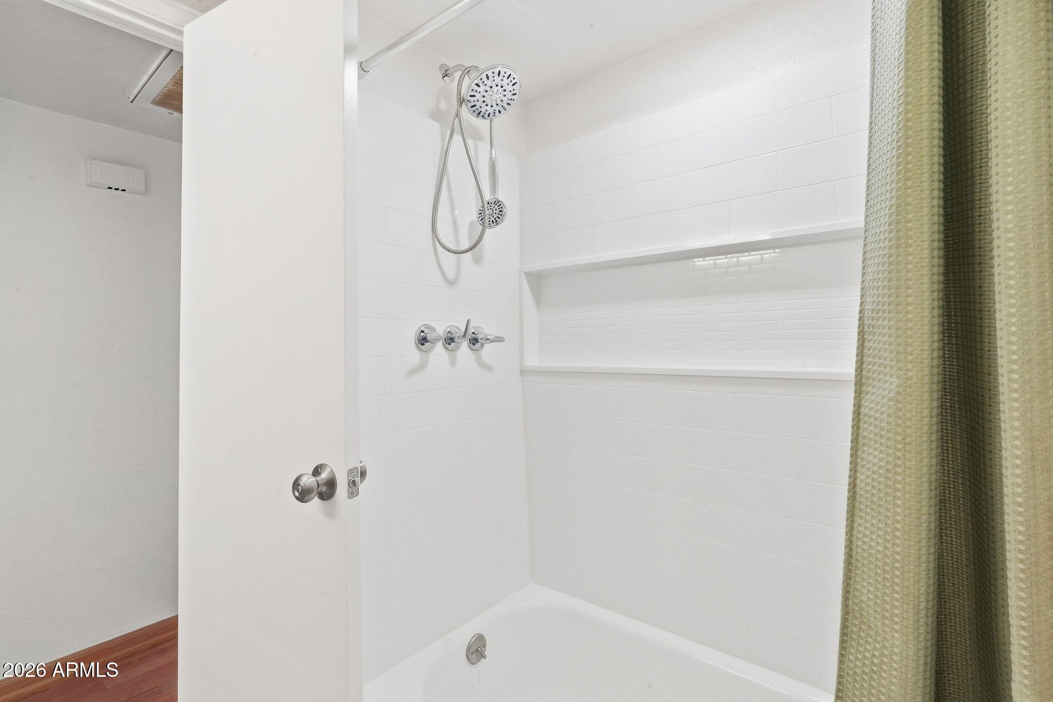 White-tiled bathtub and shower with chrome fixtures, a wide recessed niche, and a green patterned curtain.