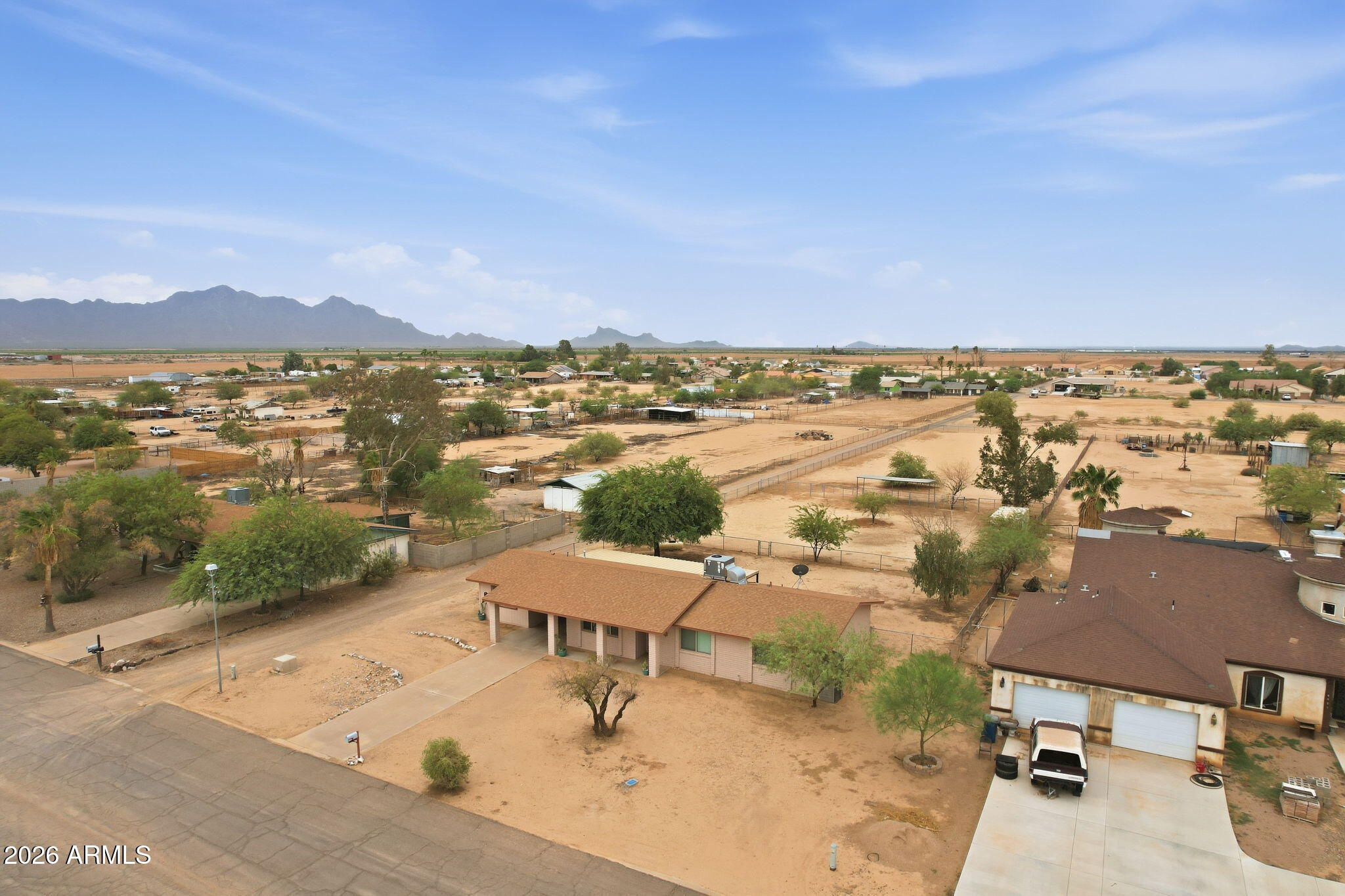 Aerial view of a desert home with fenced horse paddocks and distant mountains.