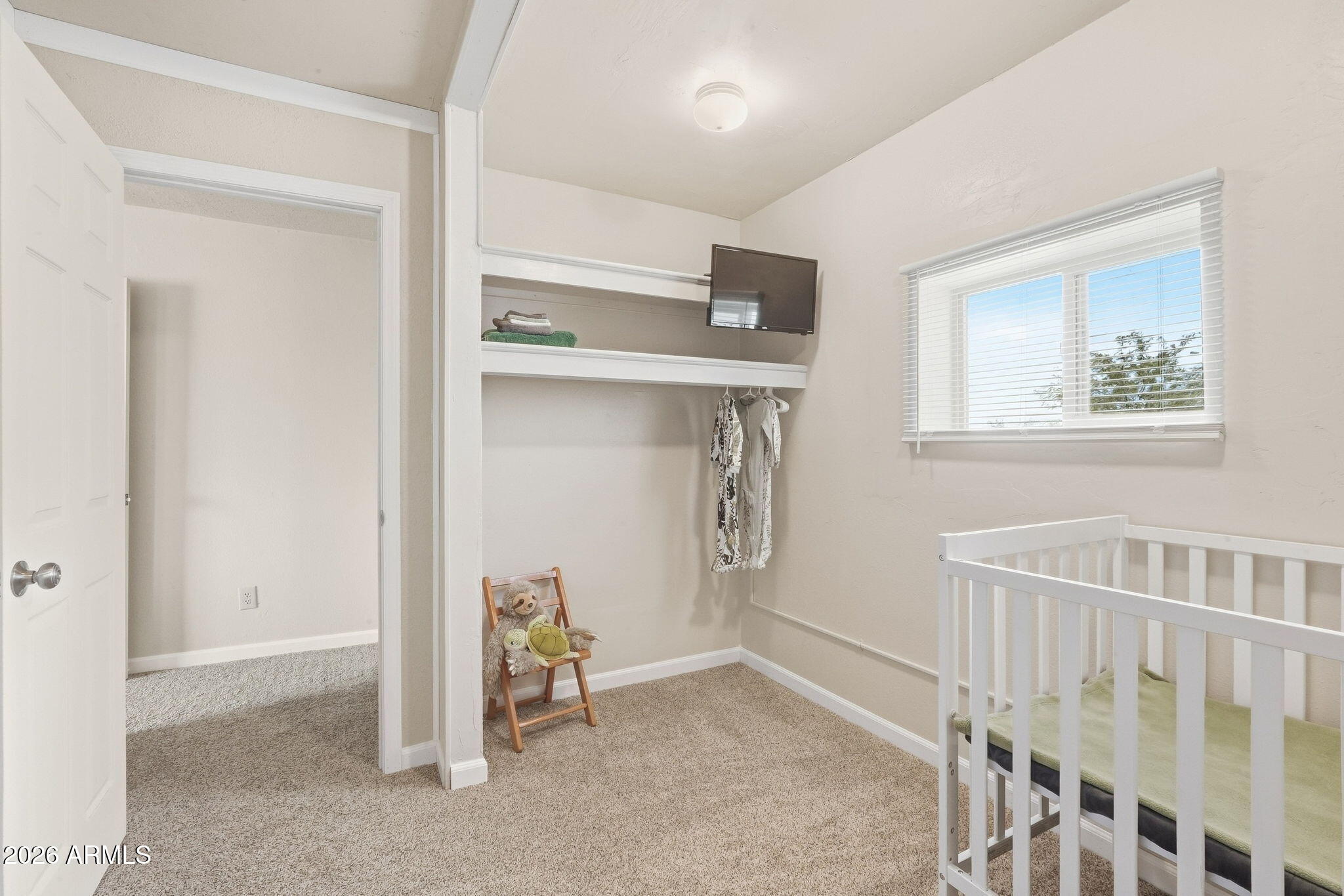 Nursery with a white crib, open clothes rail, and a small chair holding stuffed animals.