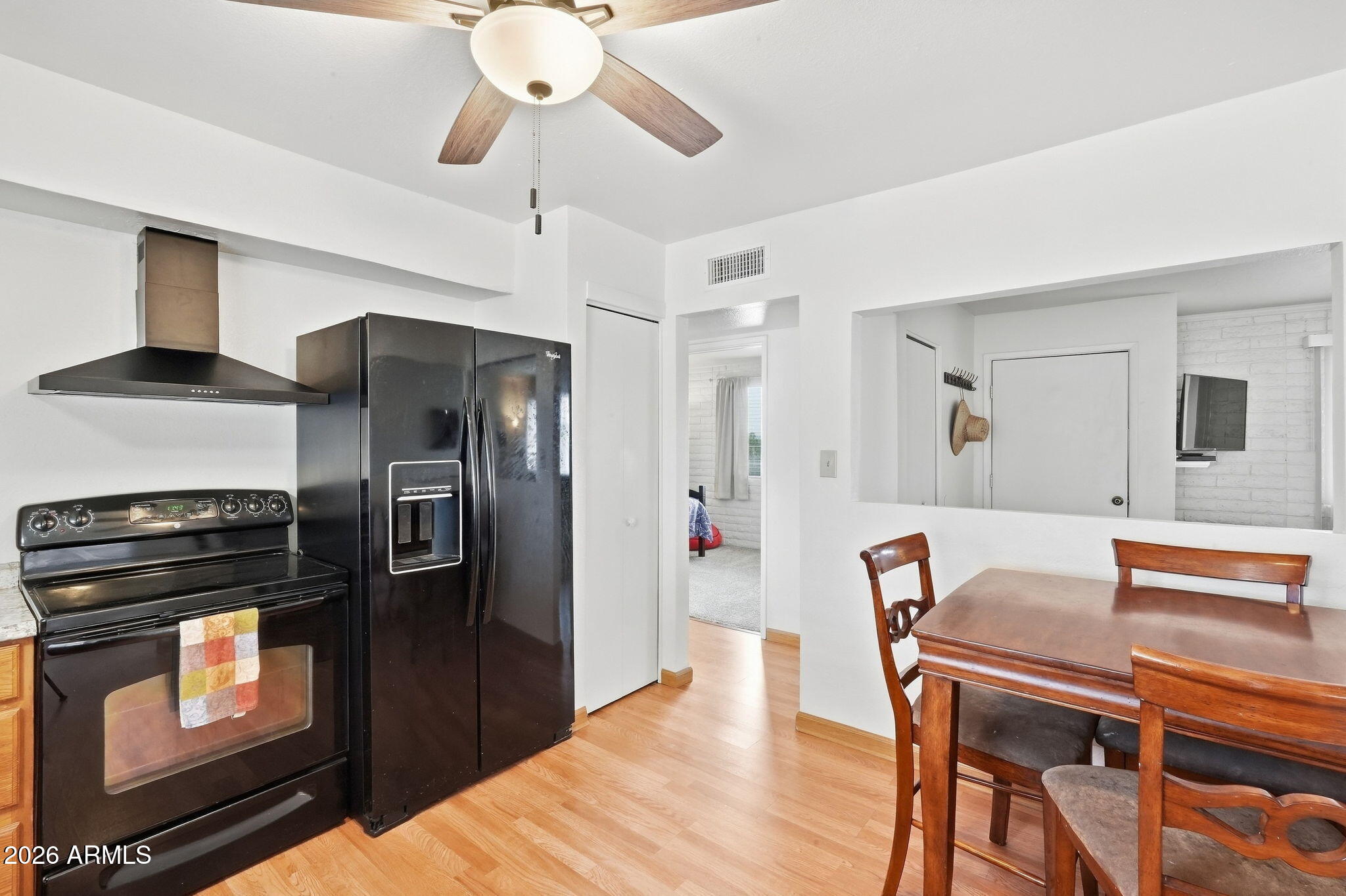 Kitchen and dining area with black appliances, wood-look flooring, and a wooden dining table.