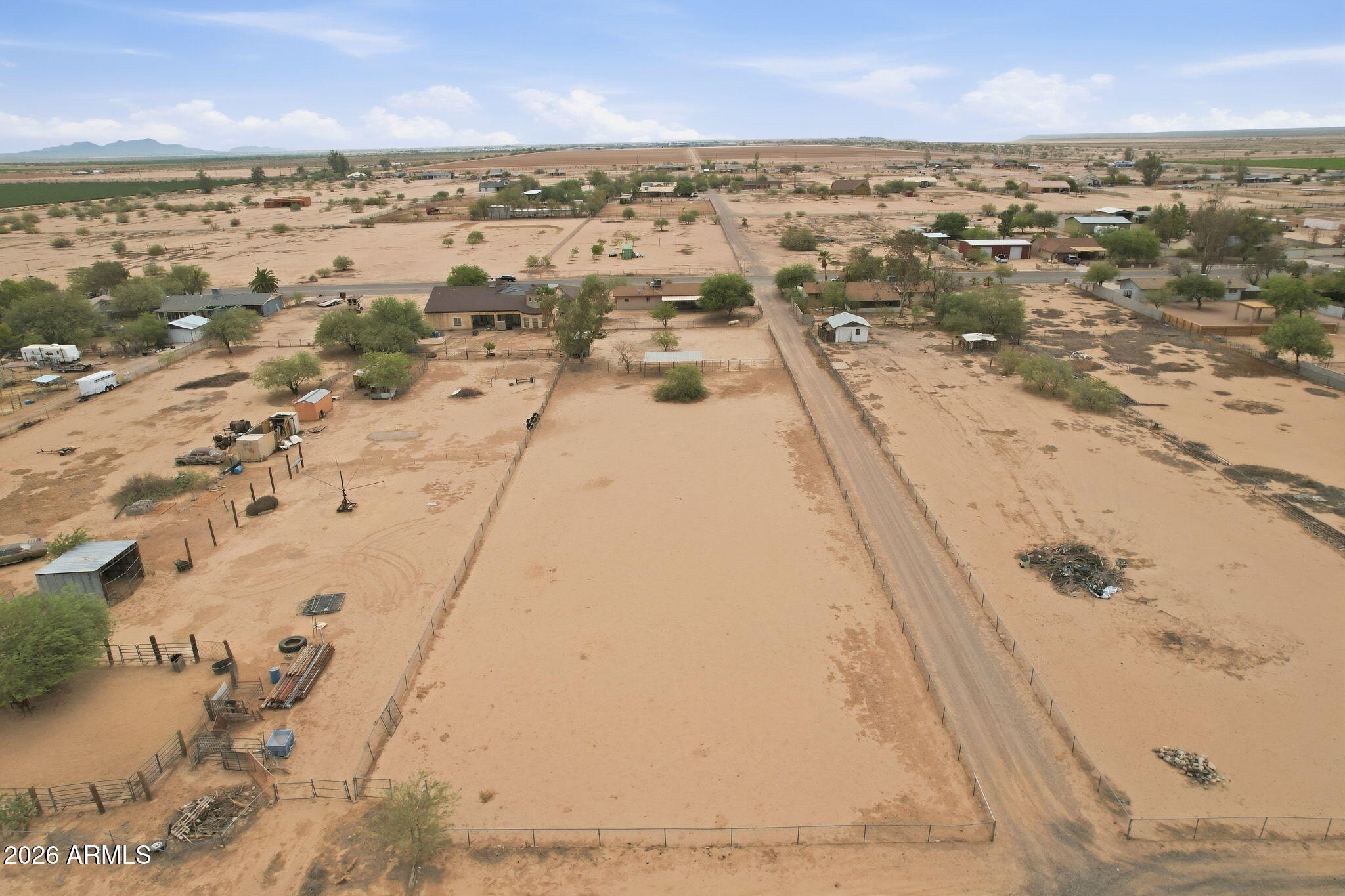 Aerial view of sandy fenced acreage with a house, outbuildings, and a long dirt road.
