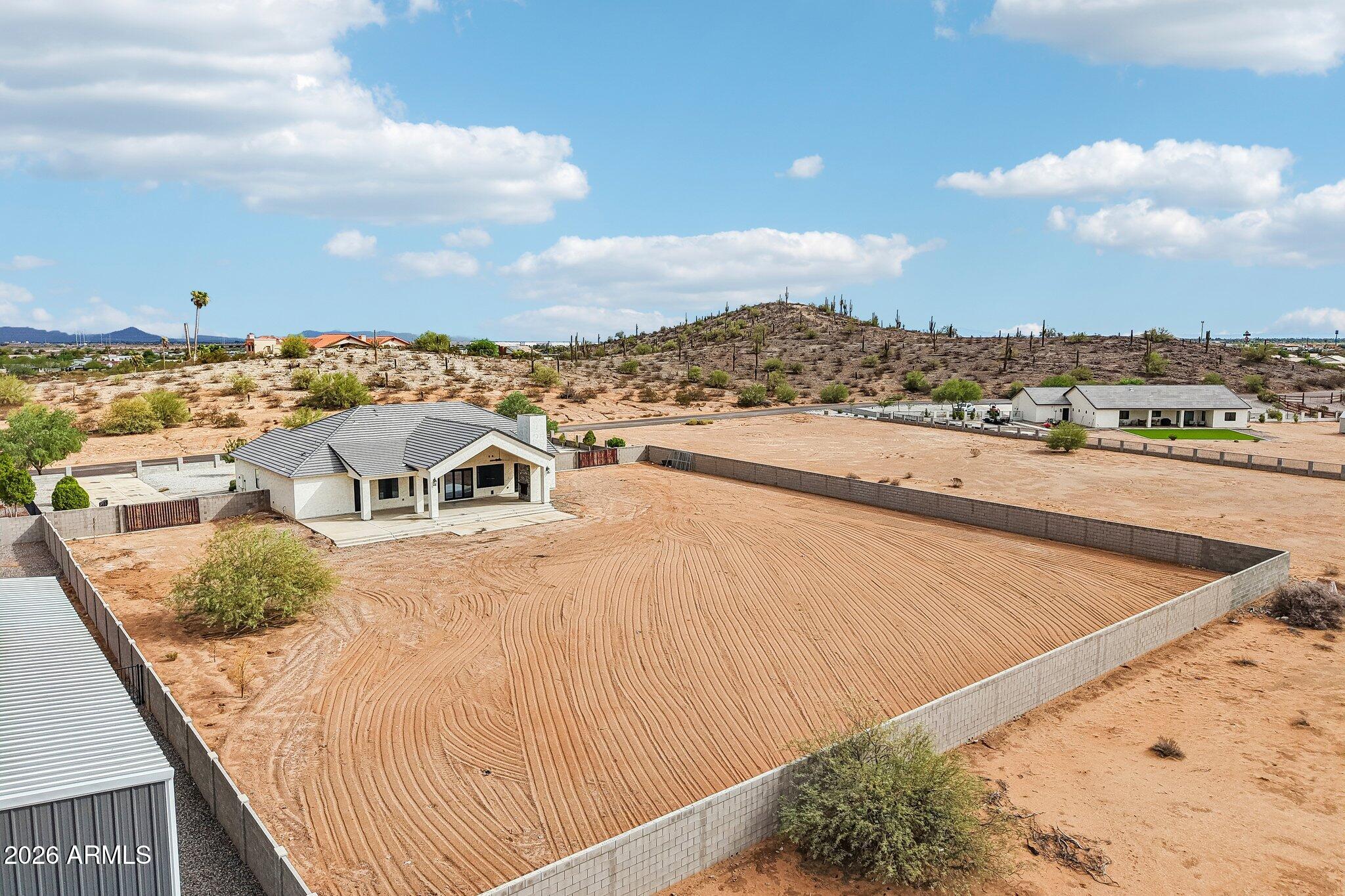 Aerial view of a desert home beside a large walled dirt yard and metal outbuilding.