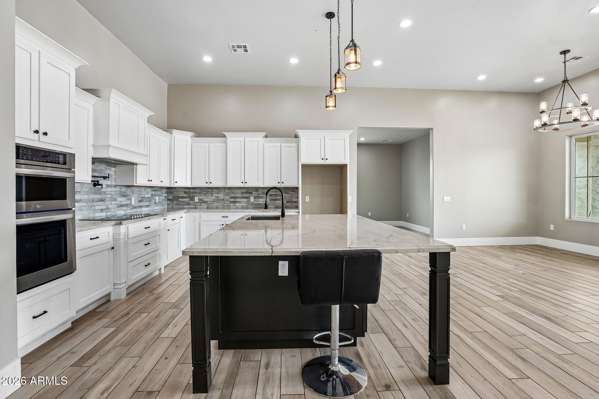 Open kitchen with white cabinets, gray tile backsplash, and a large island with a bar stool.