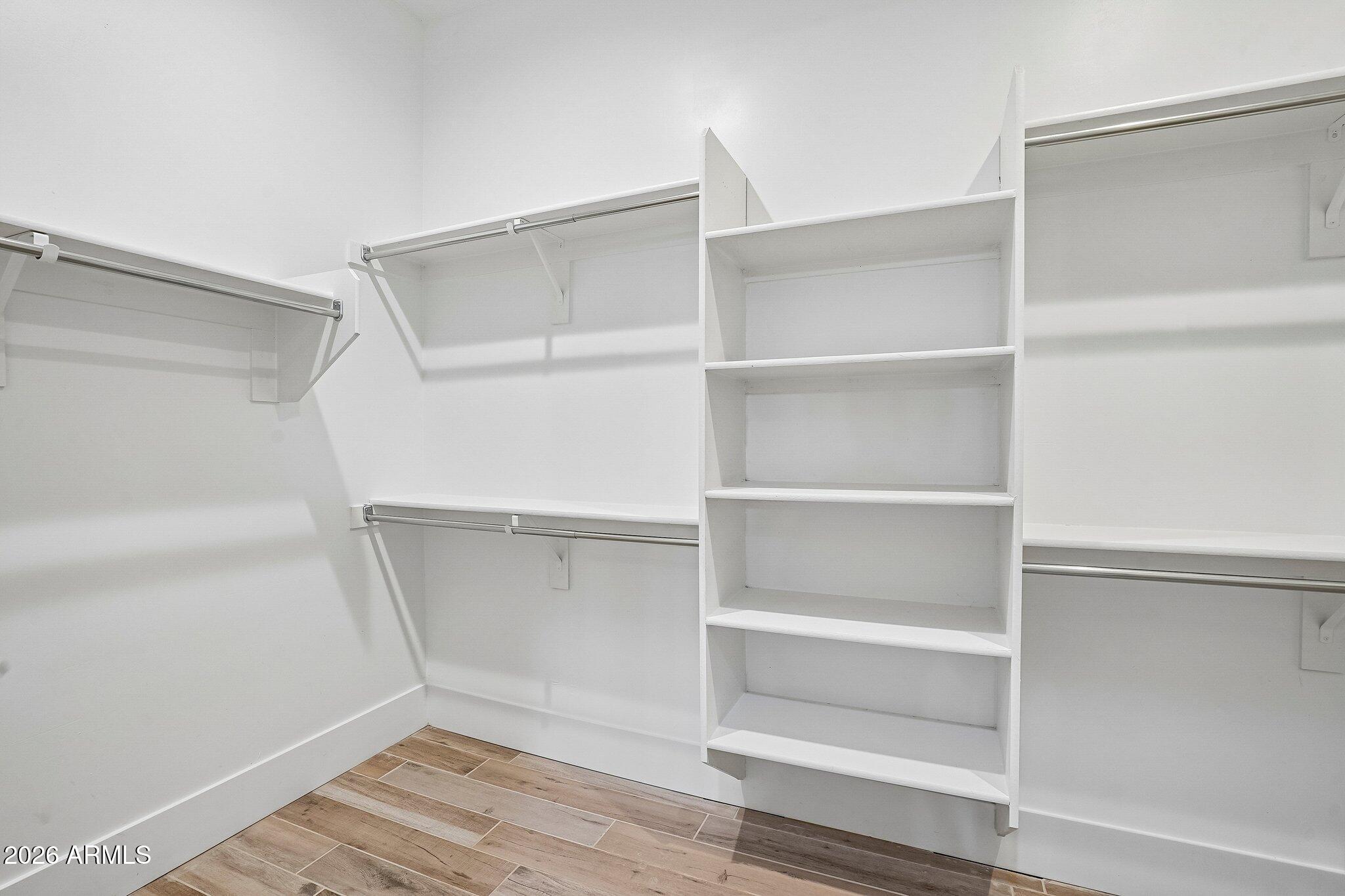 Walk-in closet with white shelving, metal hanging rods, and wood-look tile flooring.
