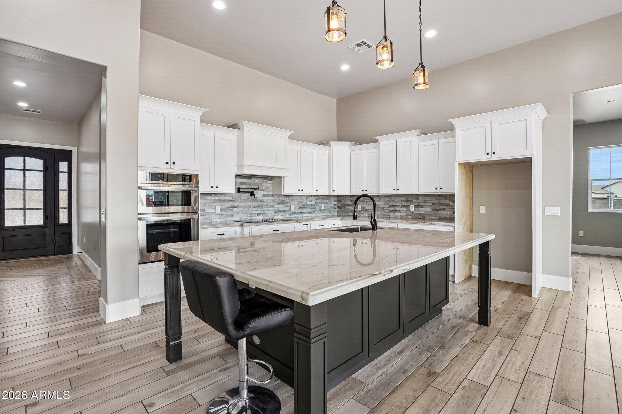 Kitchen with a large dark island, light stone countertop, white cabinets, and three pendant lights.