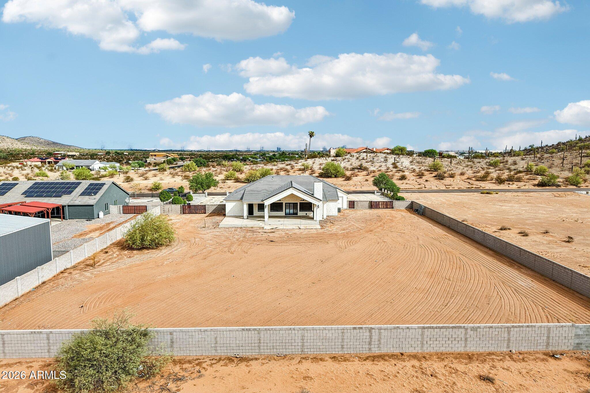Aerial view of a single-story home and broad graded dirt yard enclosed by block walls.