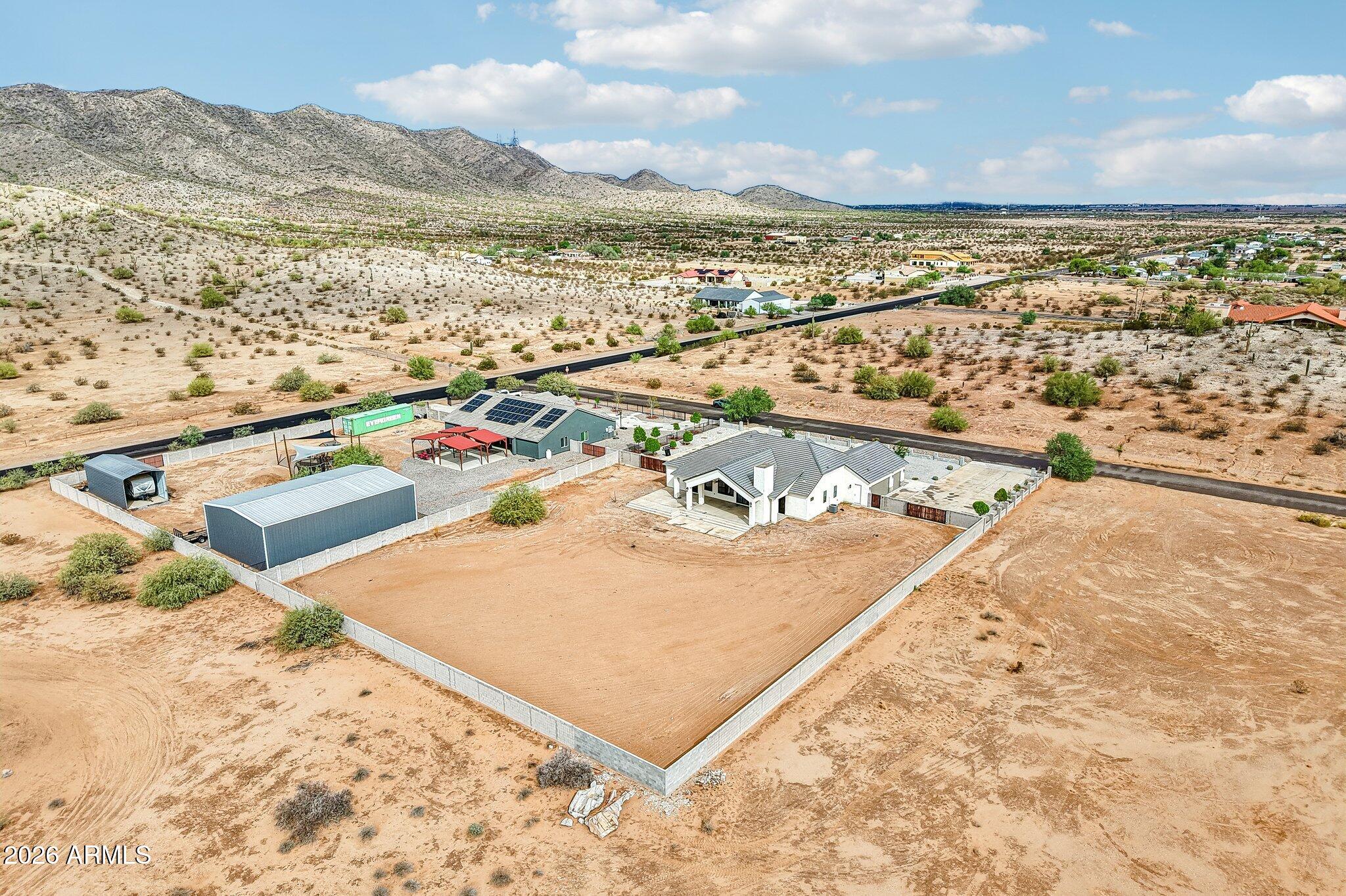 Desert horse property with a fenced riding arena, solar-paneled home, outbuildings, and mountain backdrop.