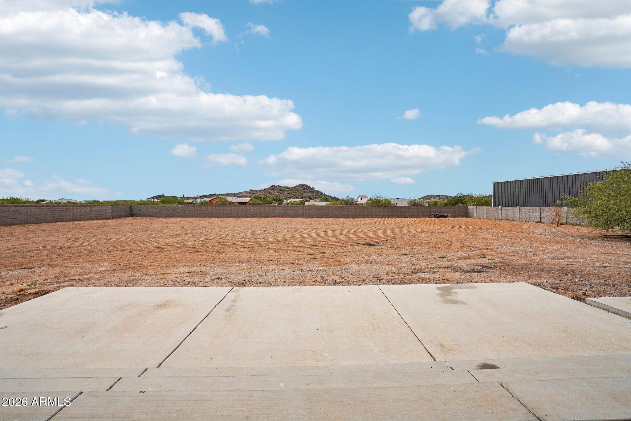 Enclosed dirt yard with a concrete patio, block walls, and a metal-sided building.