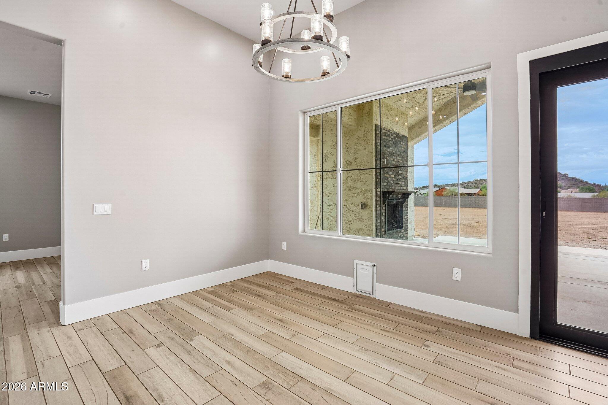 Empty dining area with plank tile flooring, a modern chandelier, and a window overlooking a patio fireplace.