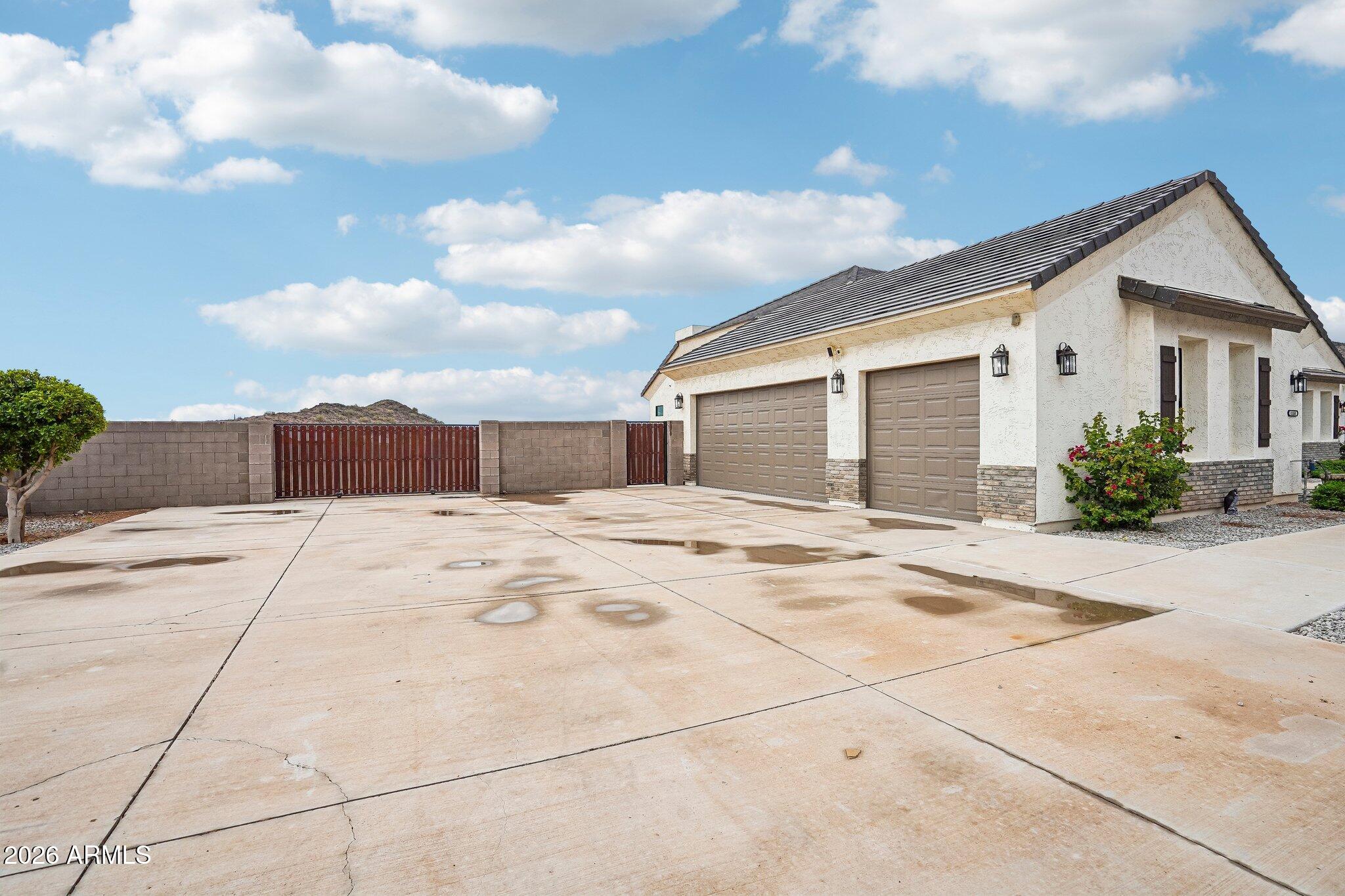 Home exterior with two garage doors, a wide concrete driveway, and a red metal gate.