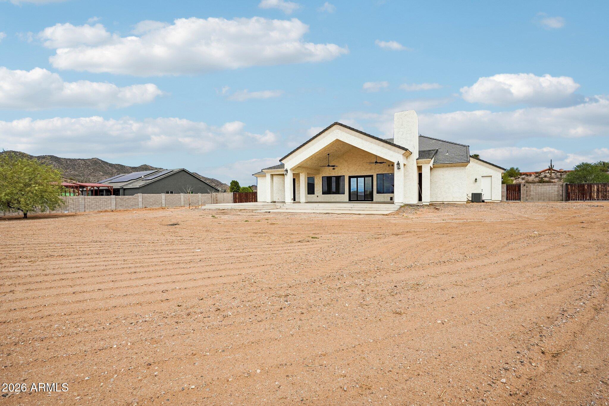 Rear exterior of a stucco home with a covered patio and broad gravel yard.