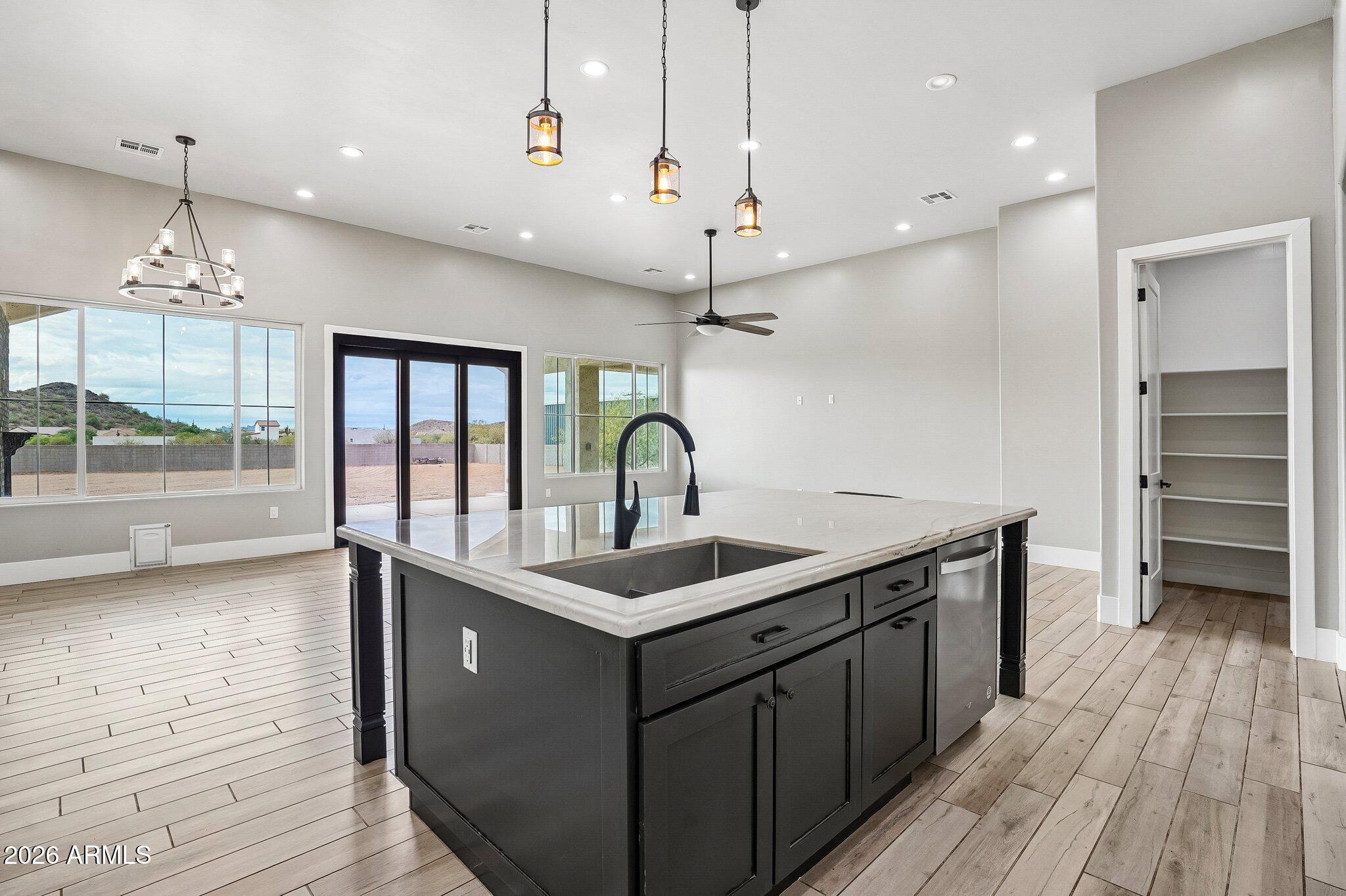 Kitchen with a large dark island, deep sink, pendant lights, and sliding glass doors.