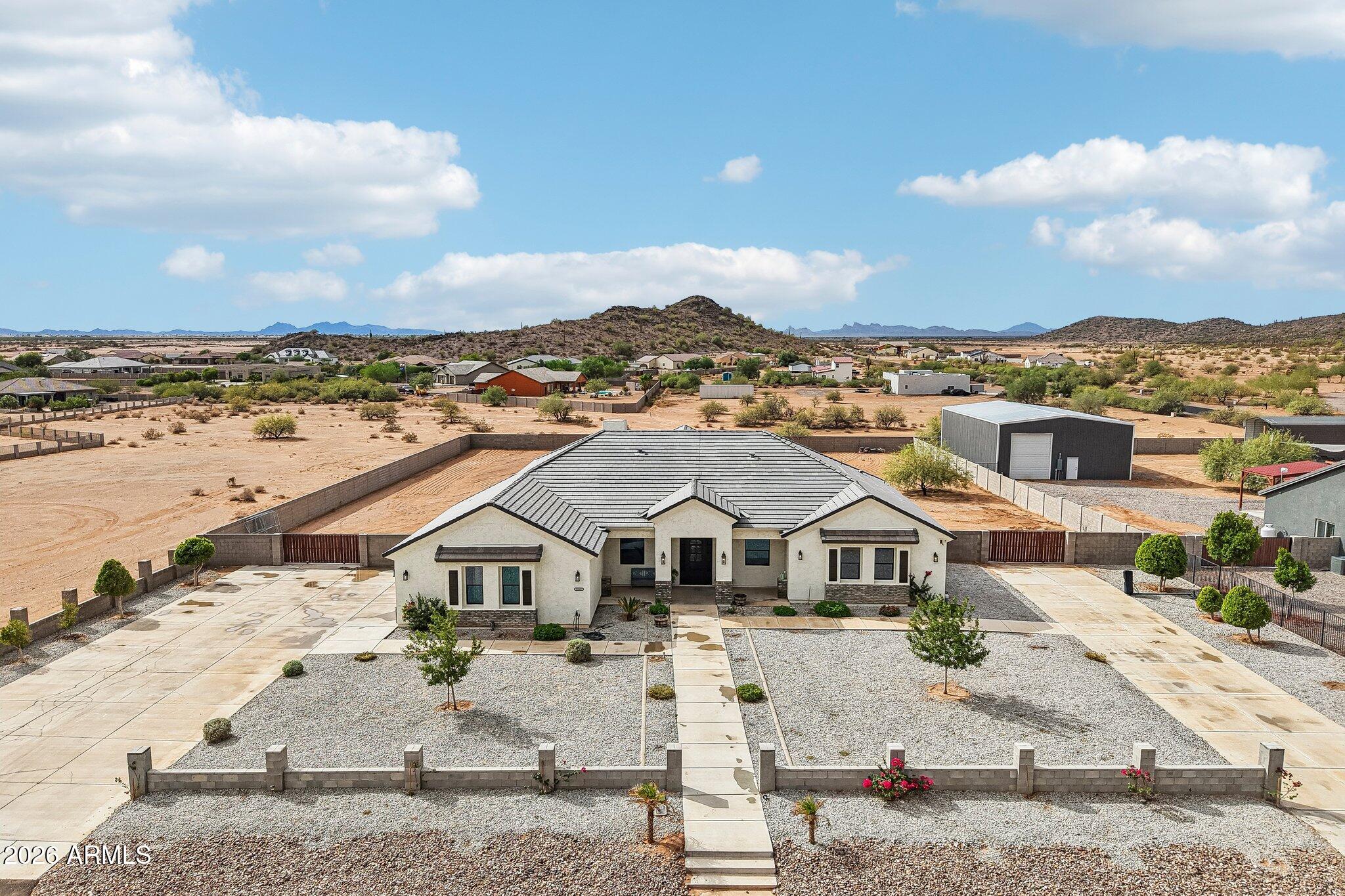 Aerial view of a single-story home on a walled desert lot with mountain views.