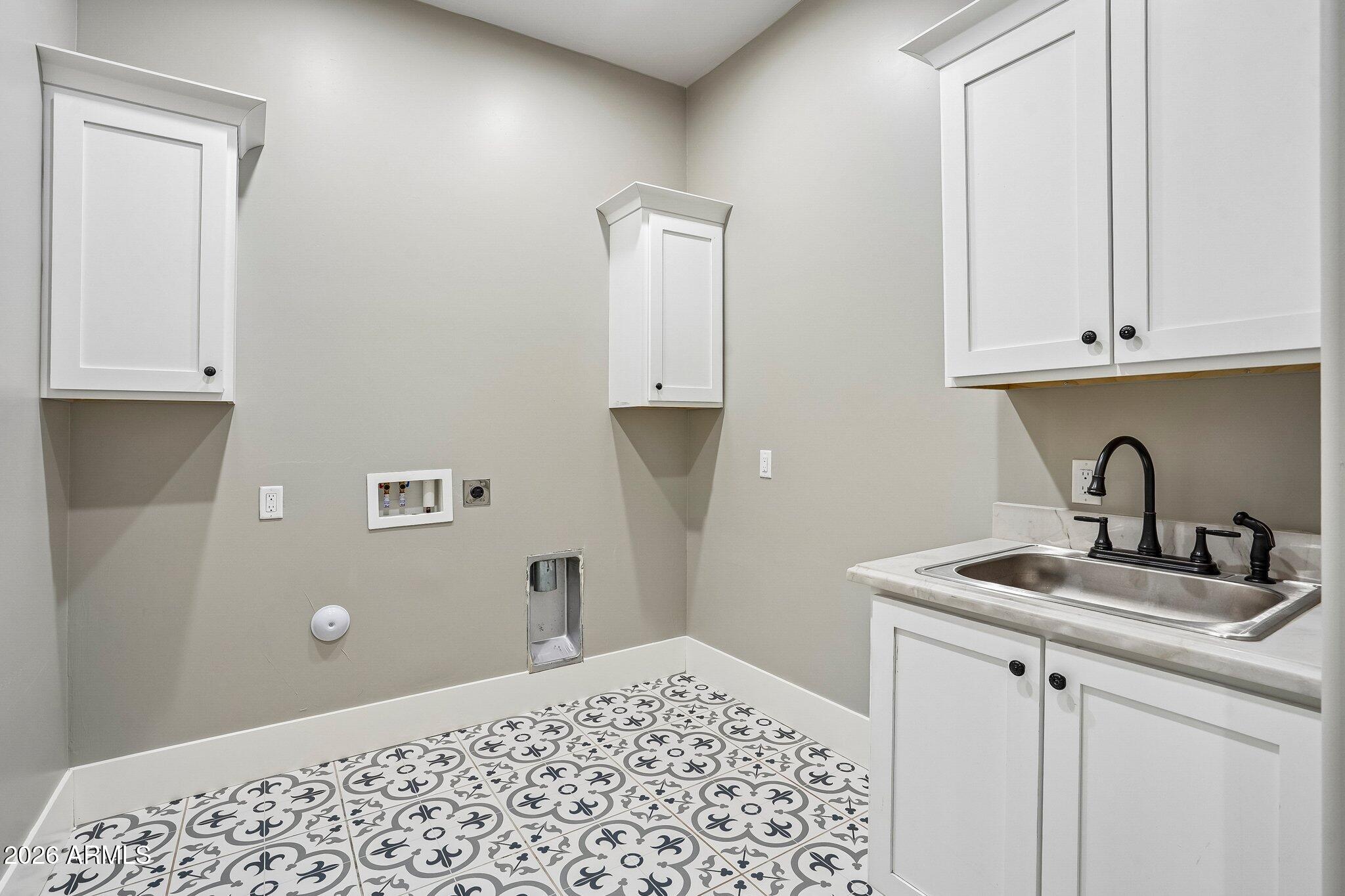 Laundry room with patterned tile floors, white cabinets, washer hookups, and a double-basin sink.