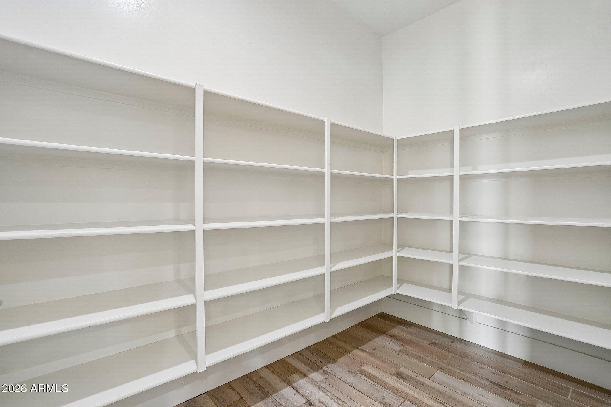 Walk-in pantry with wraparound white shelves and wood-look tile flooring.