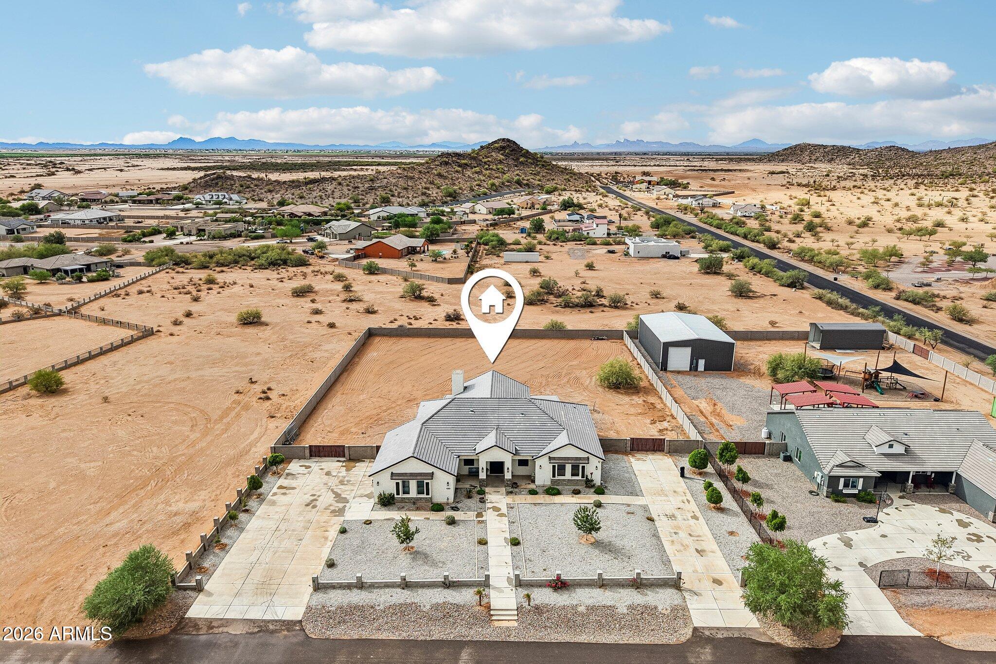 Aerial view of a desert home with a fenced yard, detached metal outbuilding, and distant mountain views.