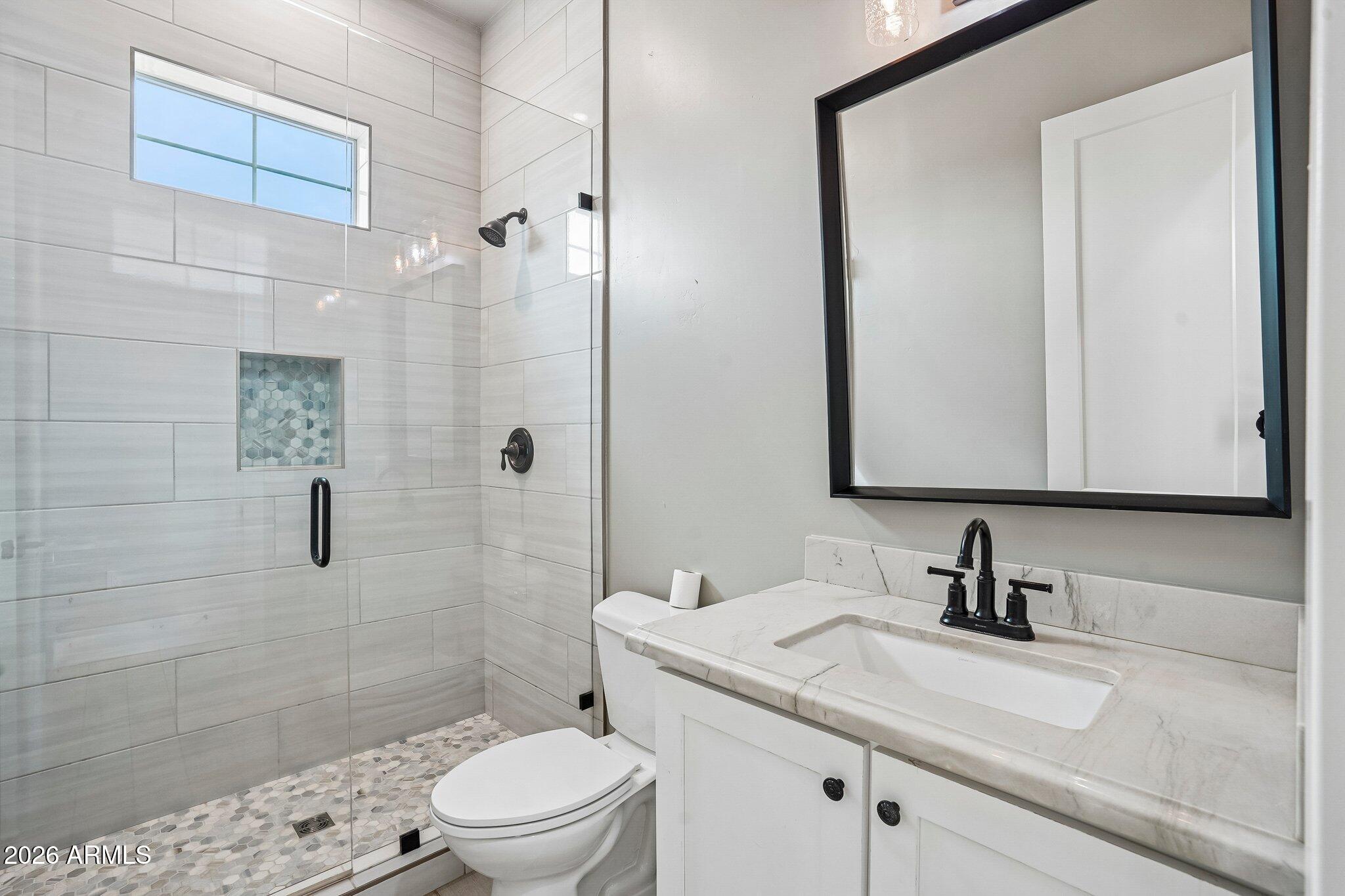 Bathroom with a tiled glass shower, mosaic niche, and white vanity with black fixtures.