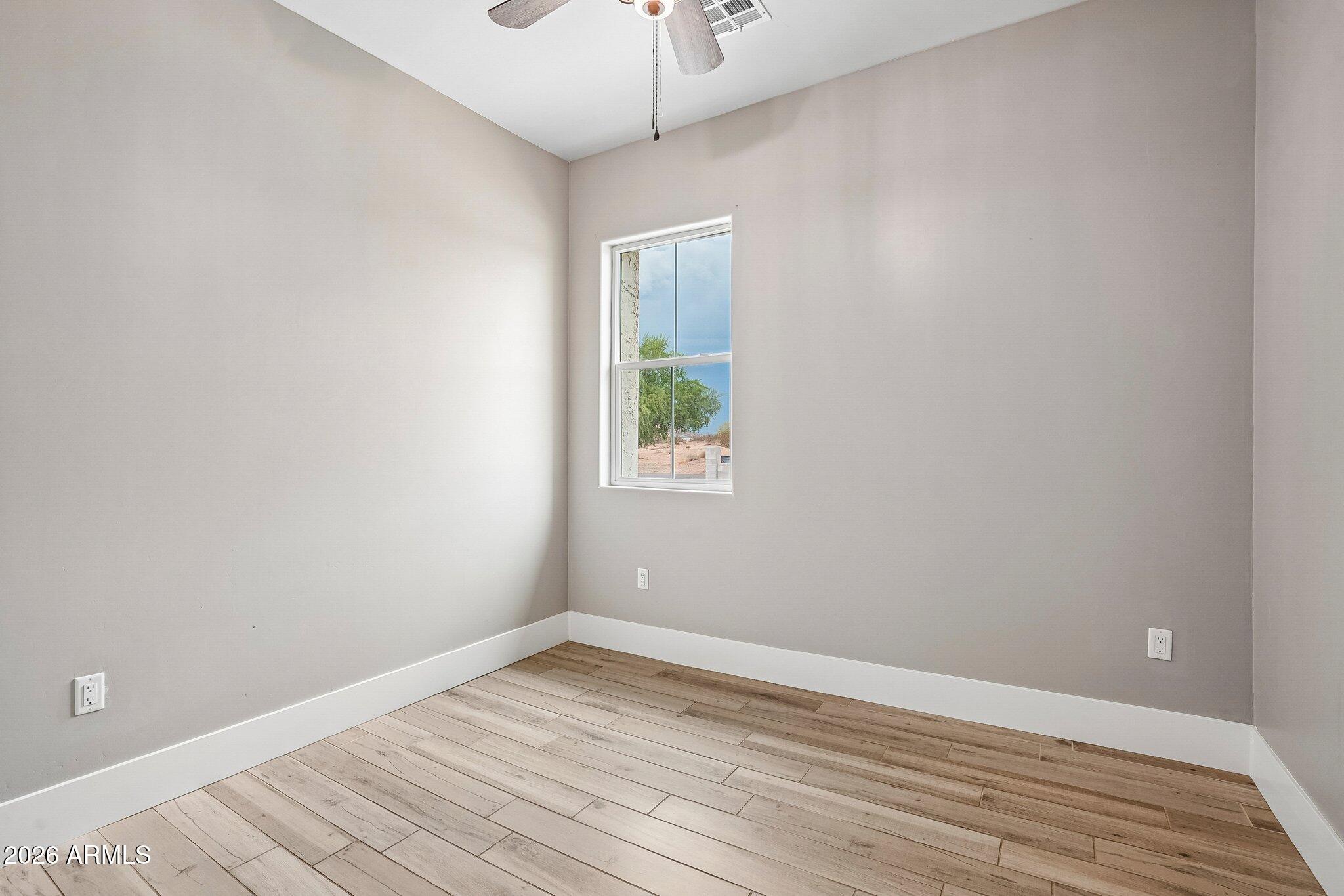 Empty room with wood-look plank flooring, a window, and a ceiling fan.