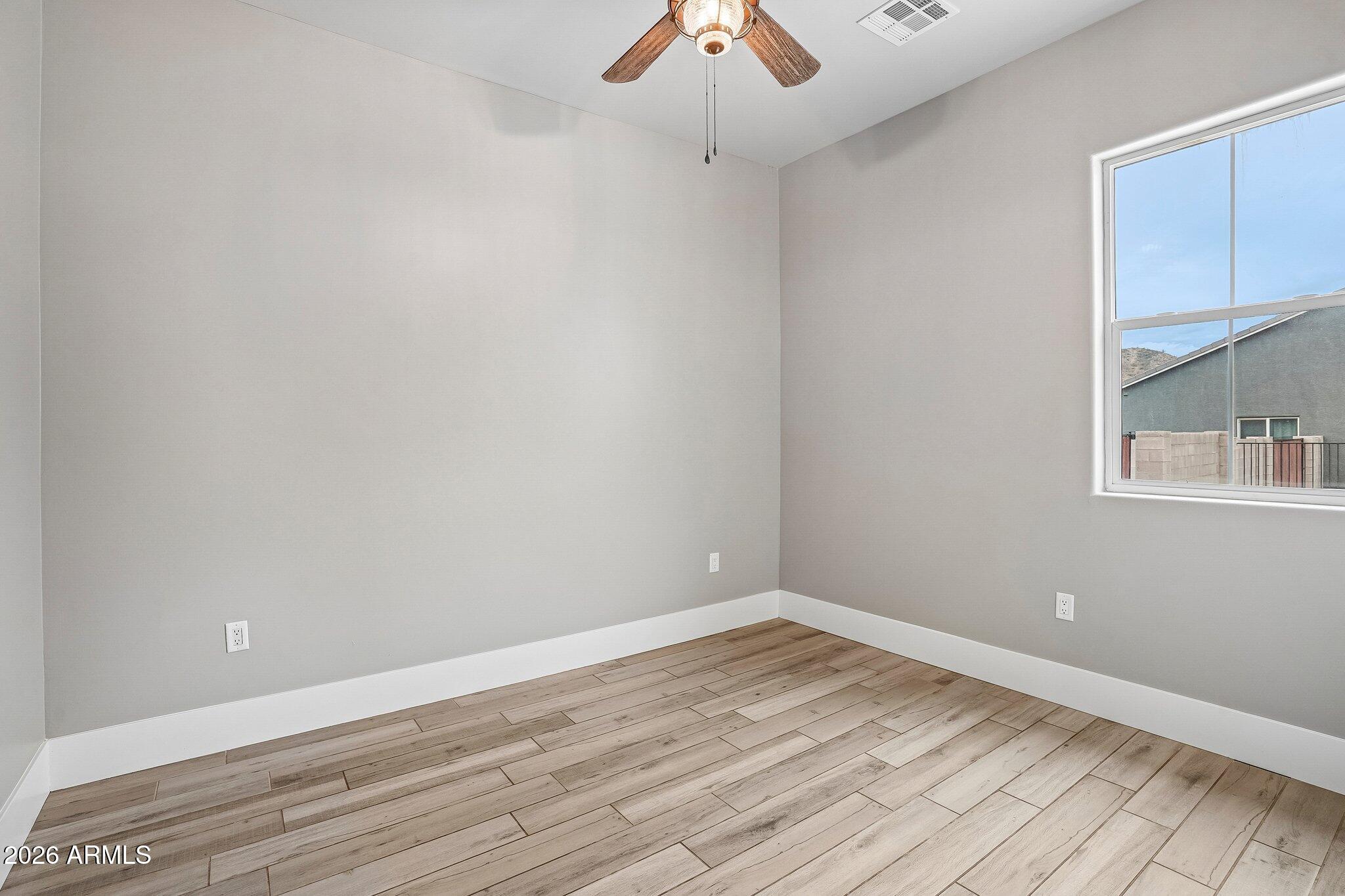 Empty room with wood-look plank flooring, a ceiling fan, and a large window.