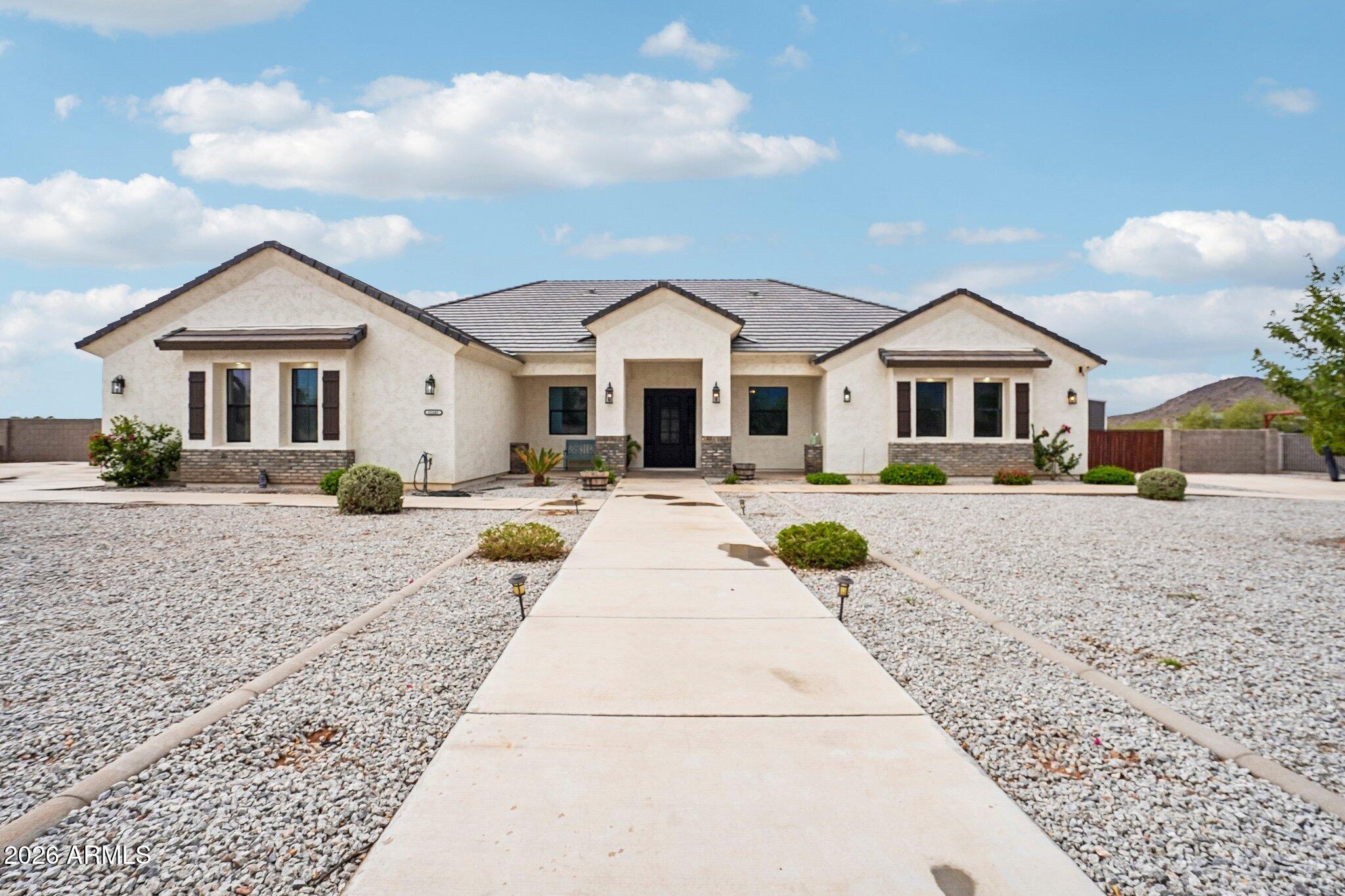 Single-story stucco home with a tiled roof, covered entry, and gravel landscaping.
