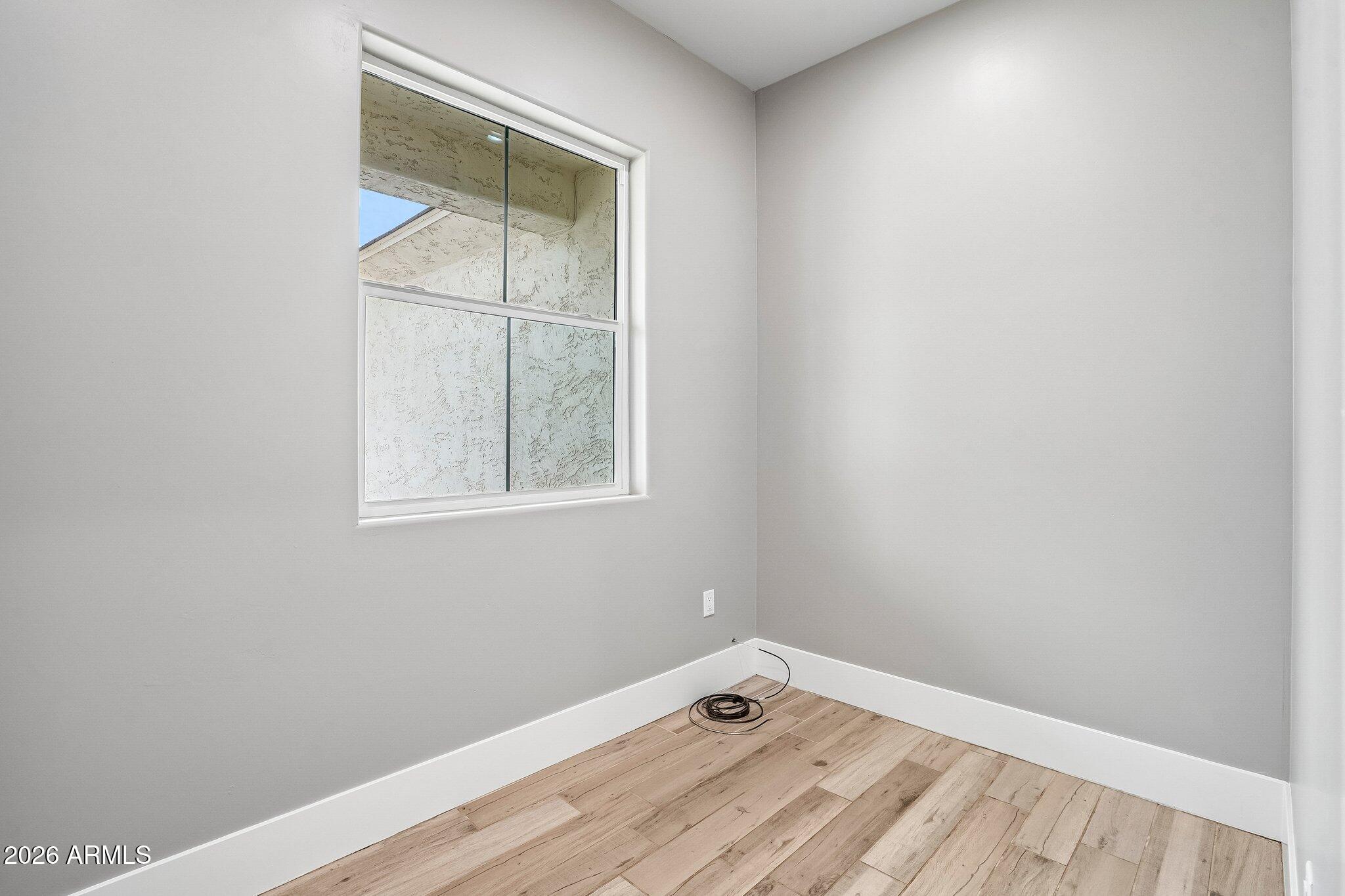 Empty room with gray walls, wood-look plank flooring, and a window facing a covered area.