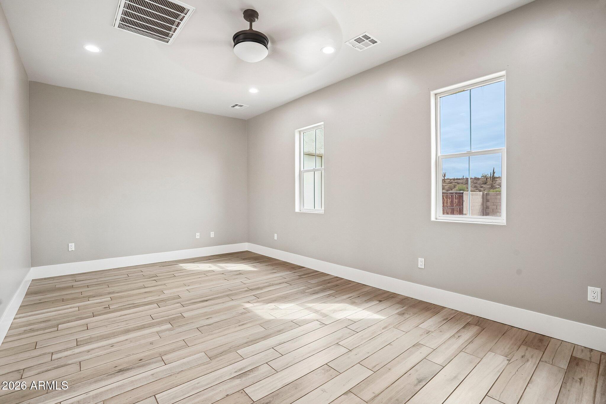 Empty bedroom with light plank flooring, two windows, and a ceiling fan.