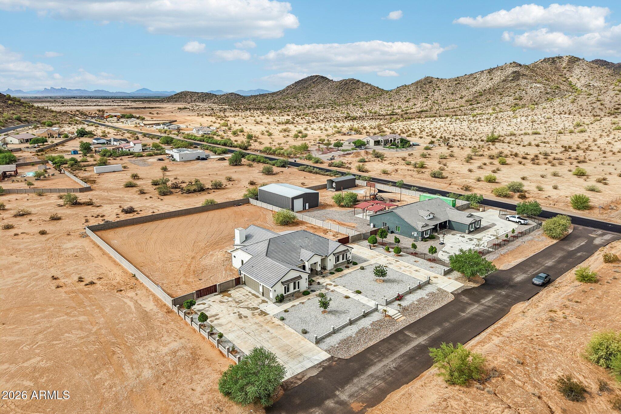 Aerial view of two homes, fenced dirt riding area, outbuildings, and surrounding Arizona desert mountains.