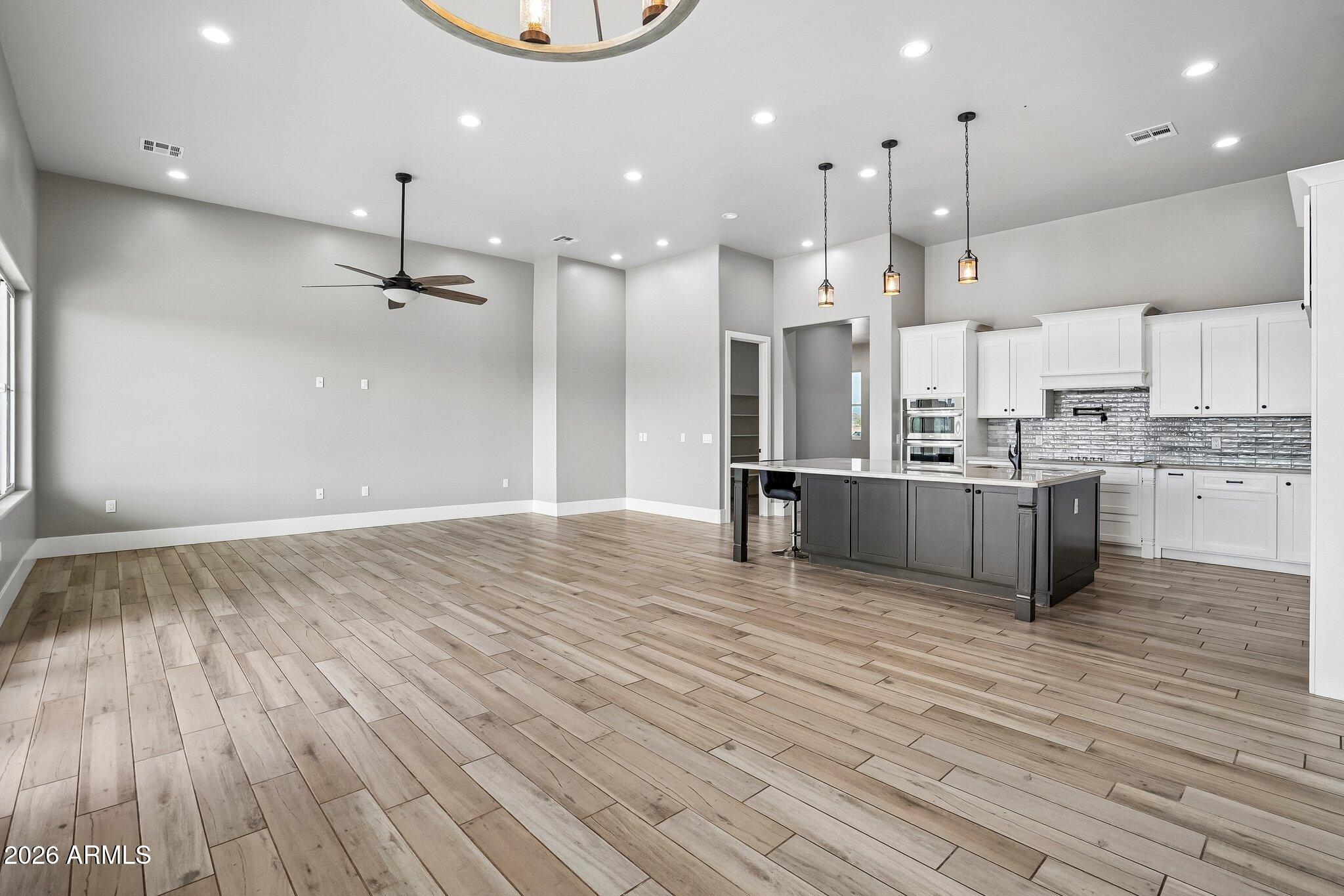 Open-plan kitchen with a dark island, white cabinets, reflective backsplash, and wood-look tile flooring.