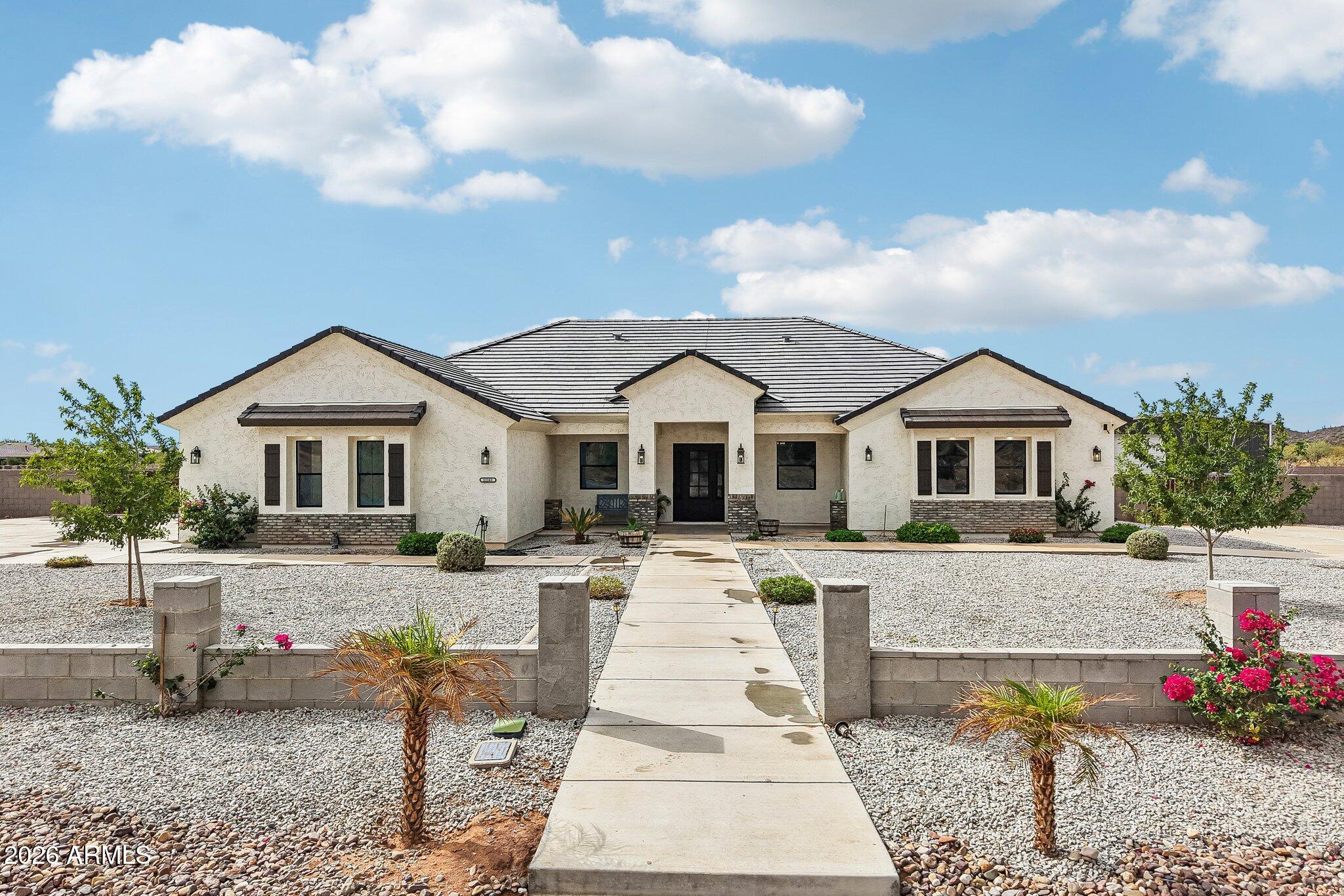 Single-story stucco home with a centered entry, gravel yard, and concrete walkway.