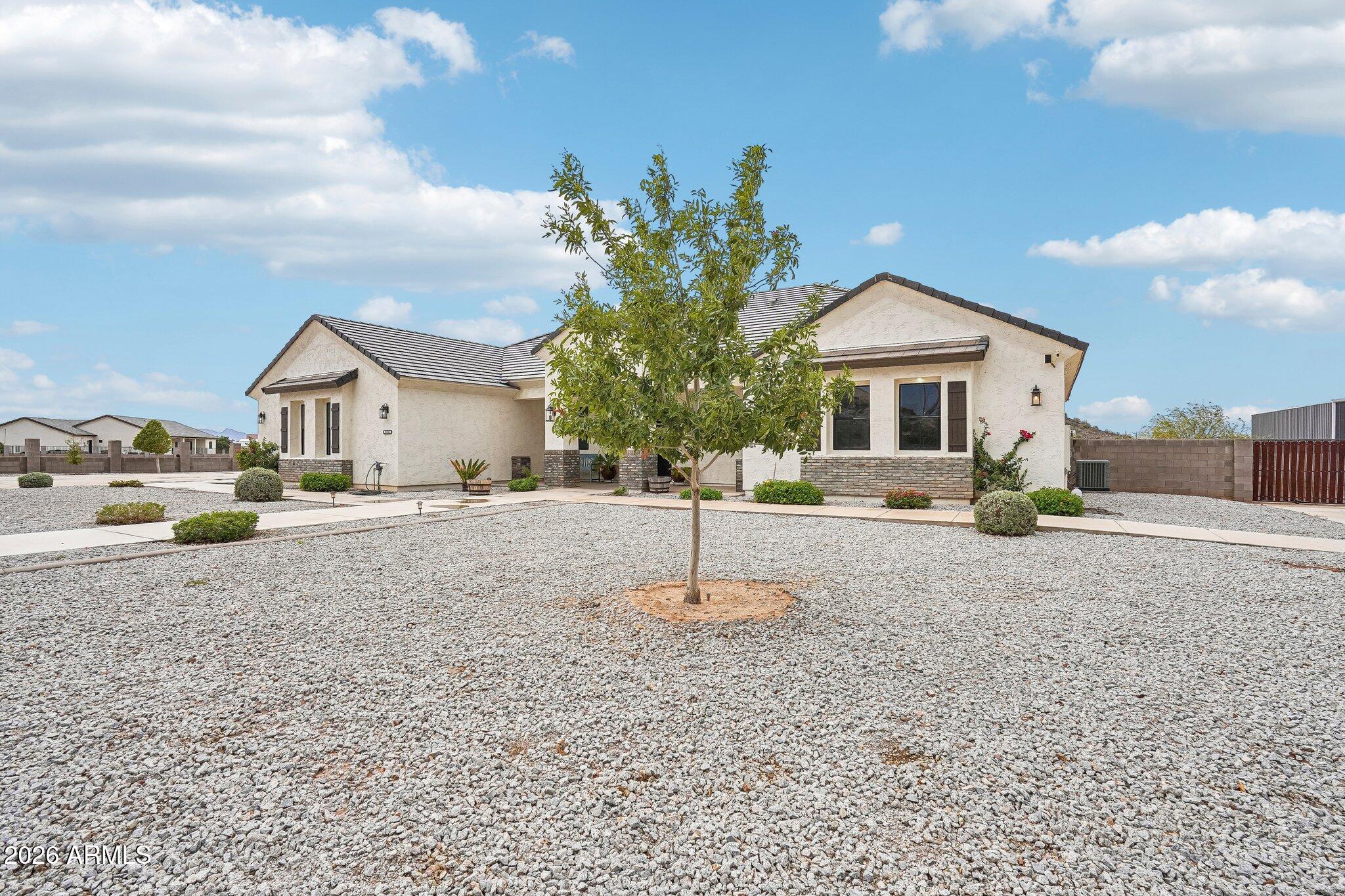 Single-story stucco home with a tile roof, gravel yard, and young tree in front.