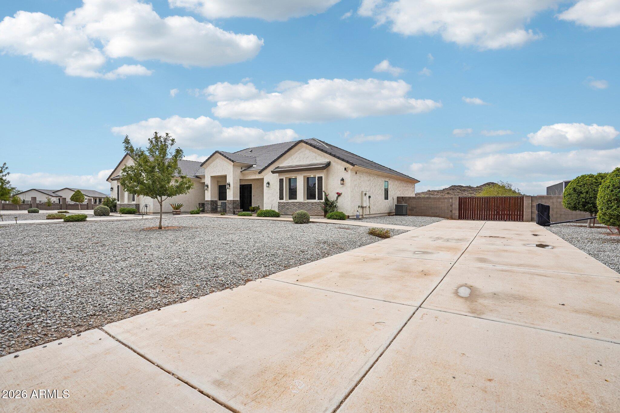 Single-story stucco home with gravel landscaping, a broad concrete driveway, and a gated side yard.