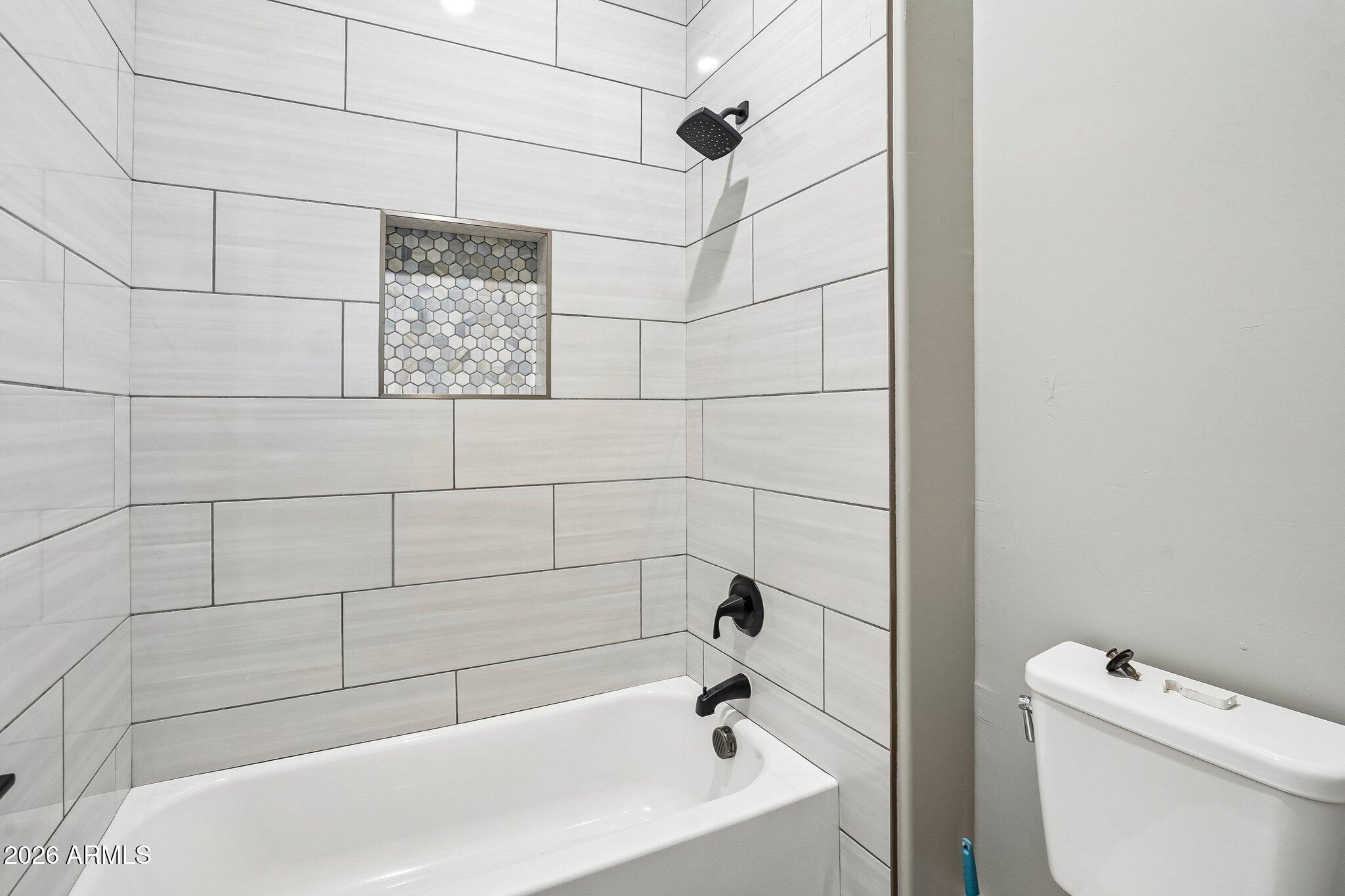 Bathroom tub and shower with white tile, a hexagonal mosaic niche, and matte black fixtures.