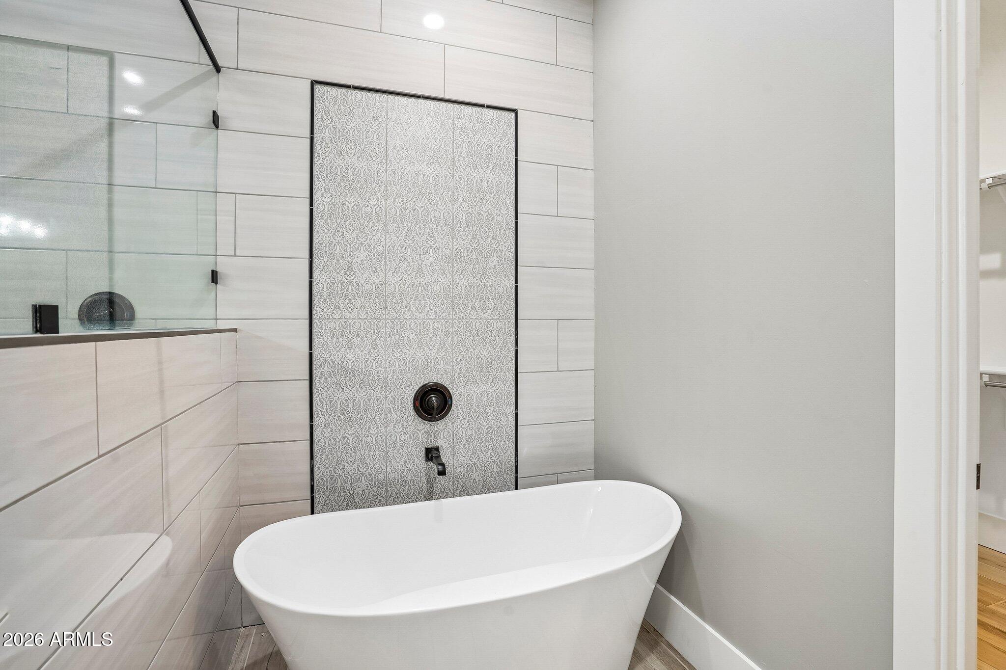 Modern bathroom with a freestanding soaking tub and glass shower featuring a patterned tile accent.