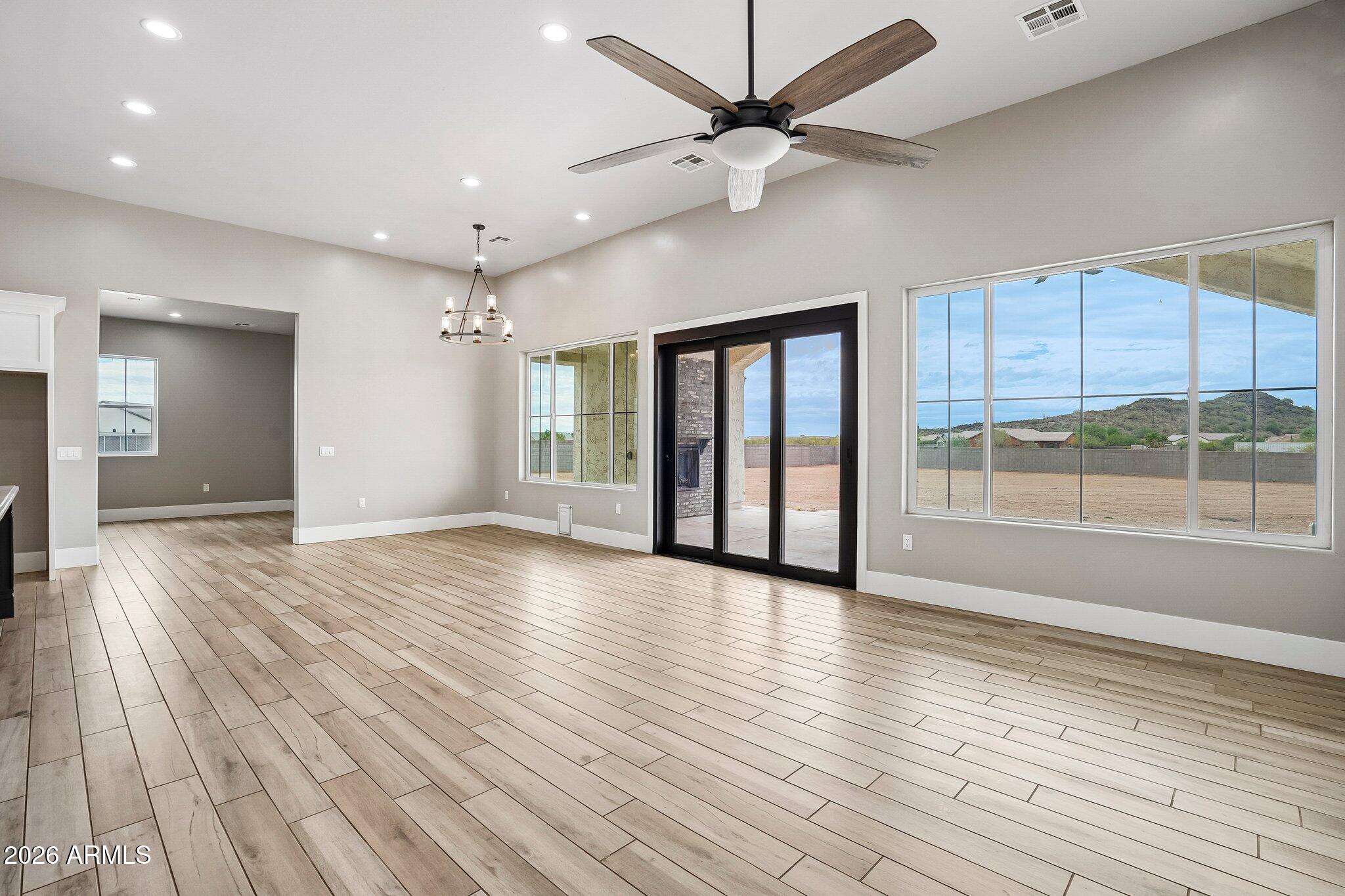 Vacant living room with wood-look tile floors, a ceiling fan, and large windows facing the yard.