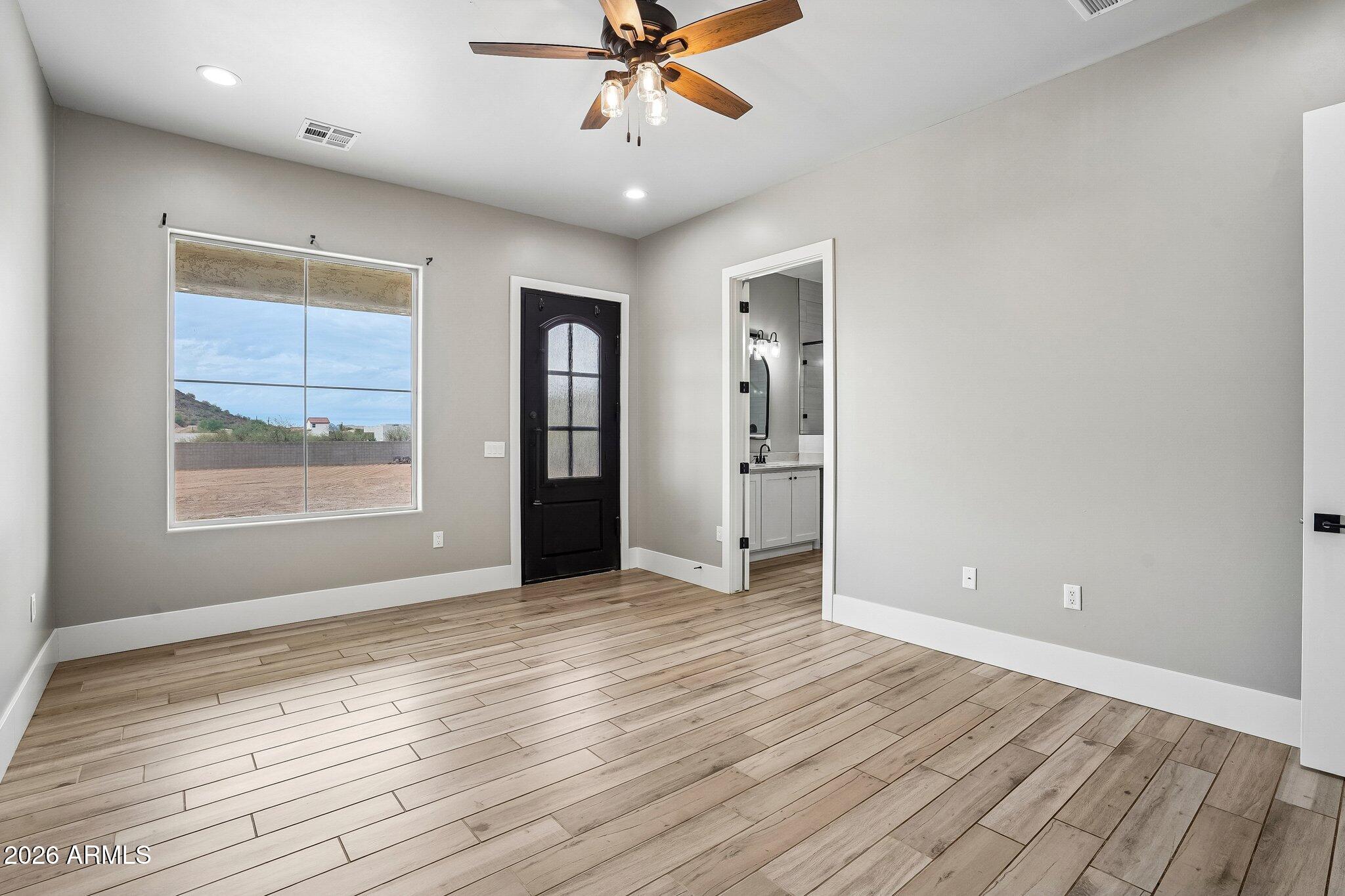 Empty room with wood-look flooring, a black door, large window, and adjoining bathroom.