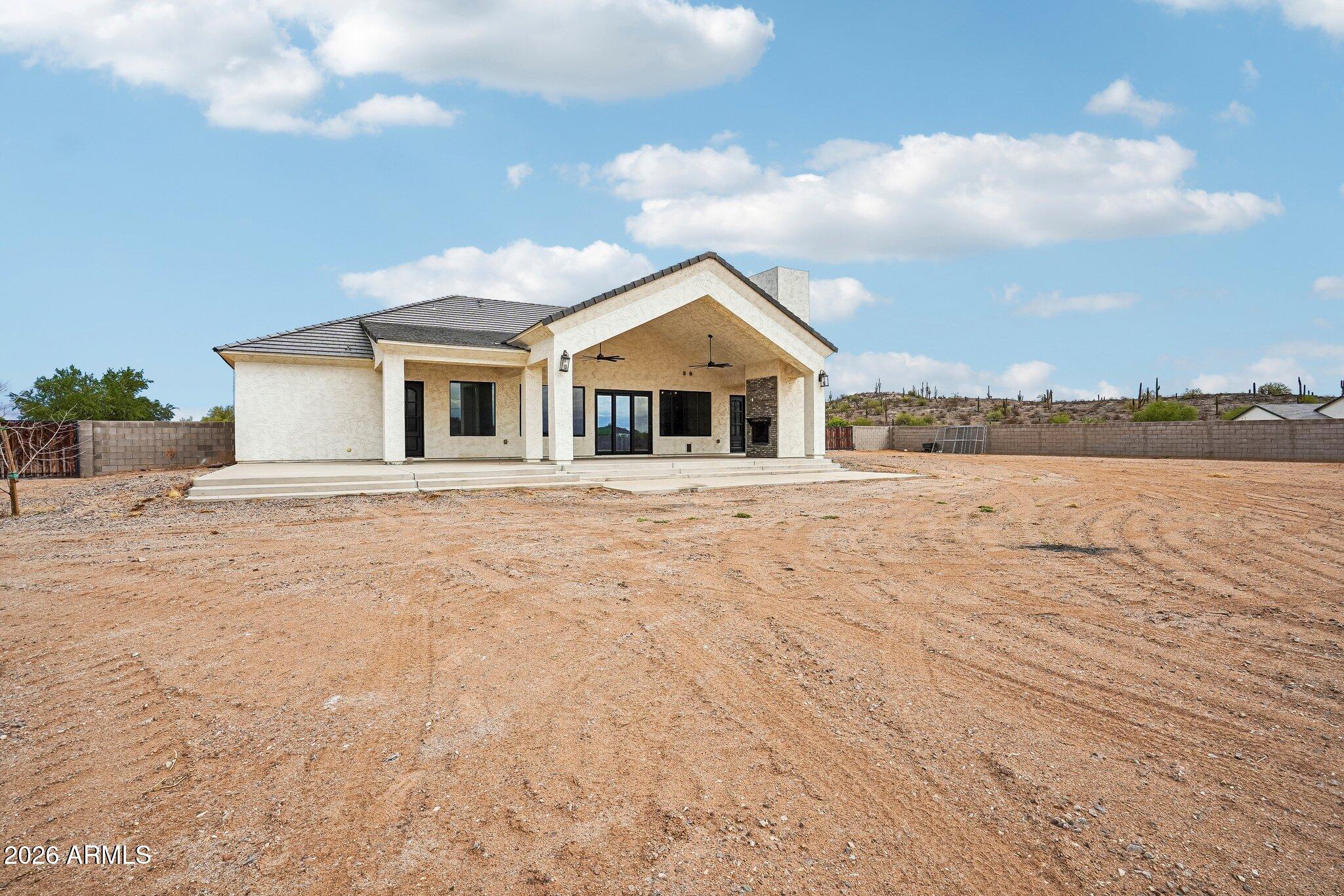 Stucco home with a covered patio and broad, bare dirt yard.
