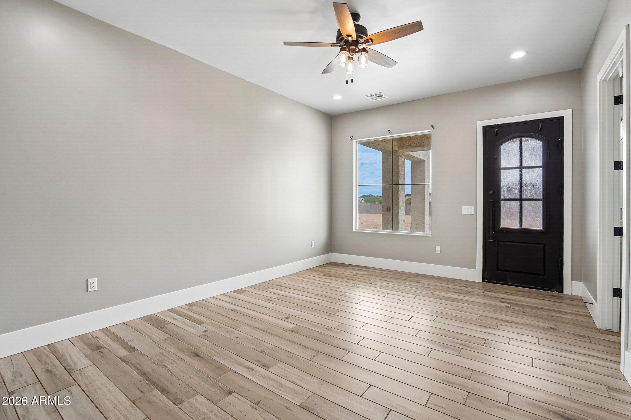 Empty entry room with wood-look tile flooring, black front door, and ceiling fan.