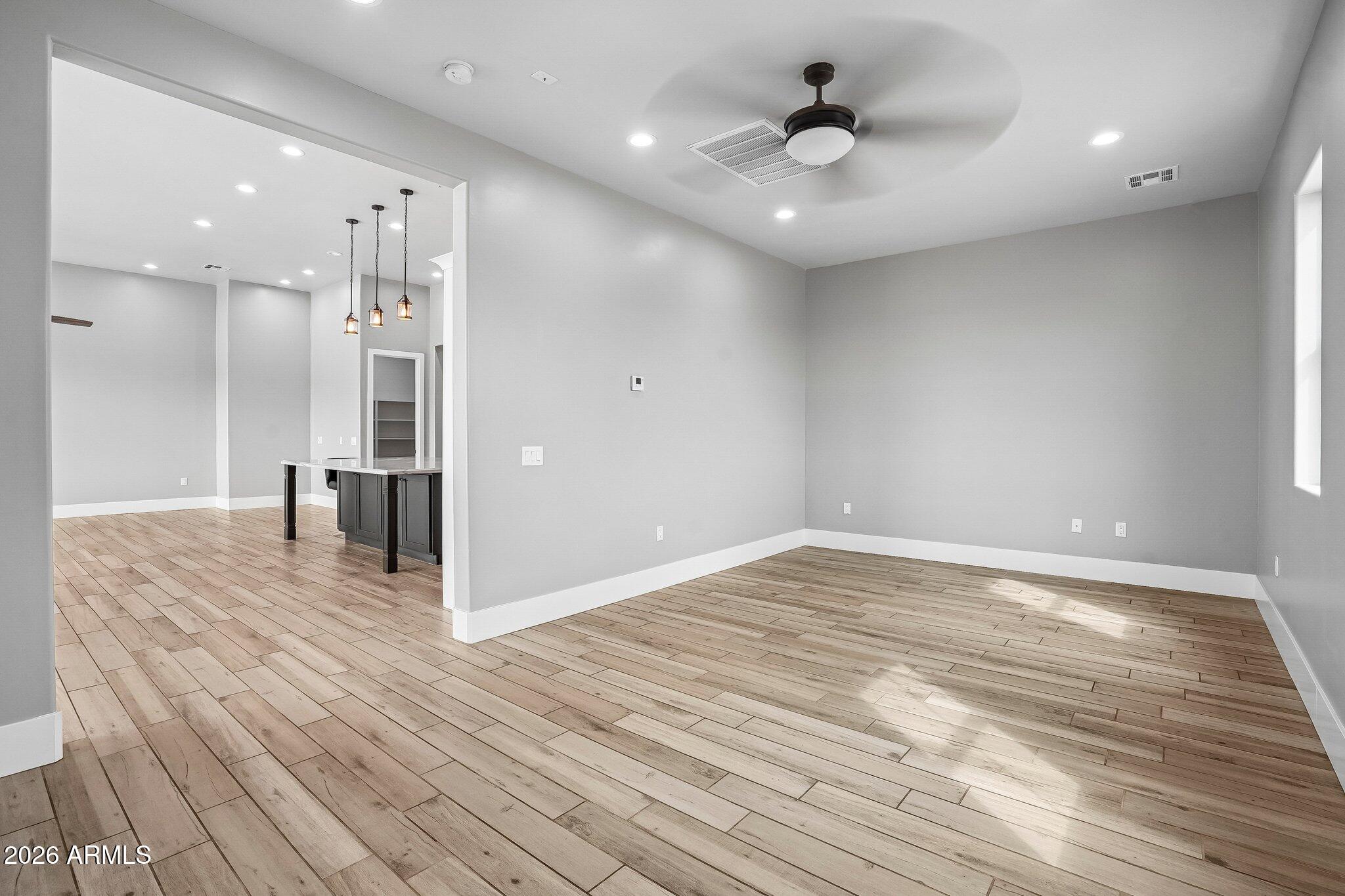 Empty living area with wood-look tile flooring, a ceiling fan, and an adjoining kitchen island.