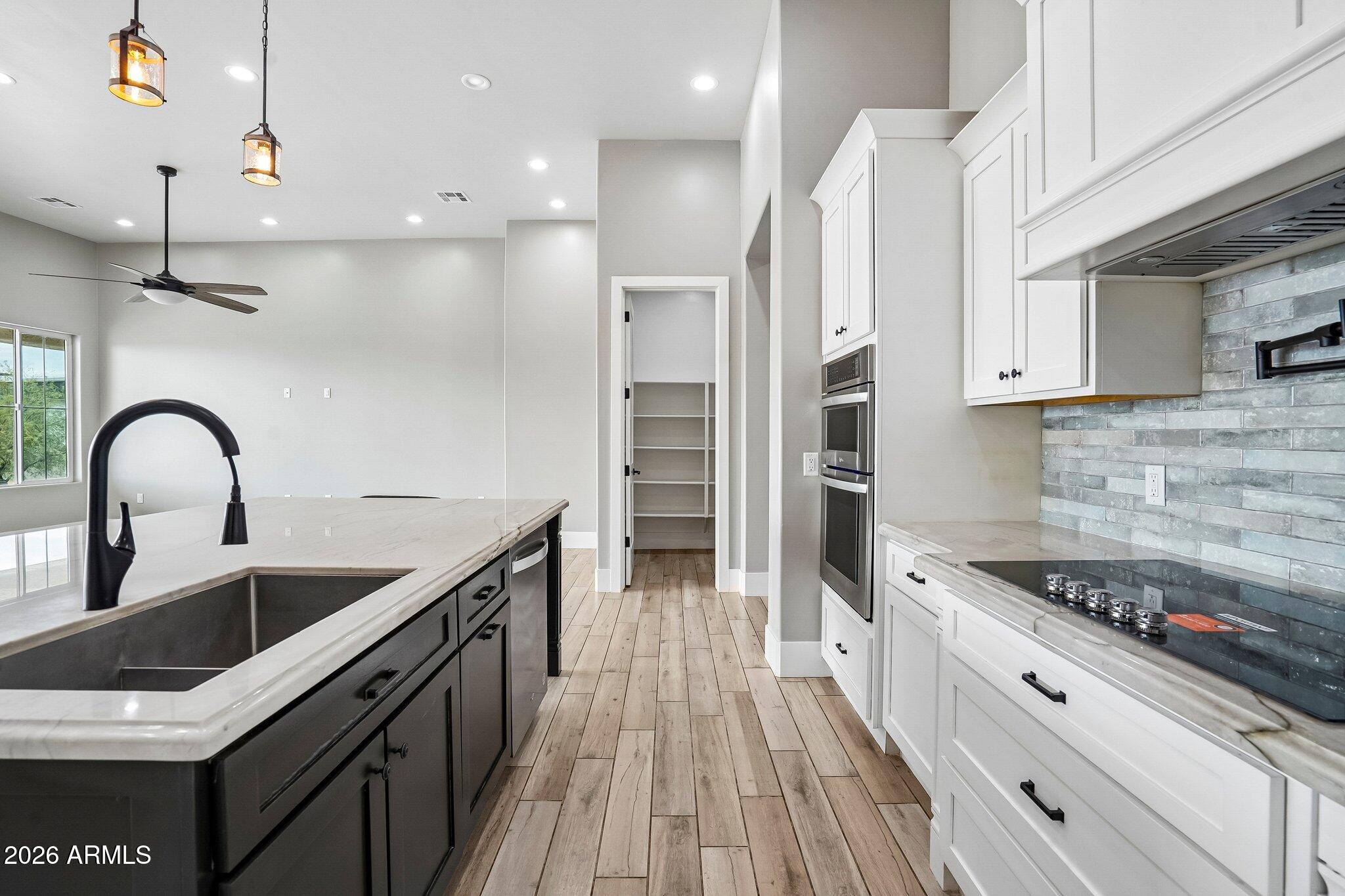 Kitchen with a large dark island, white cabinetry, gray tile backsplash, and double wall ovens.