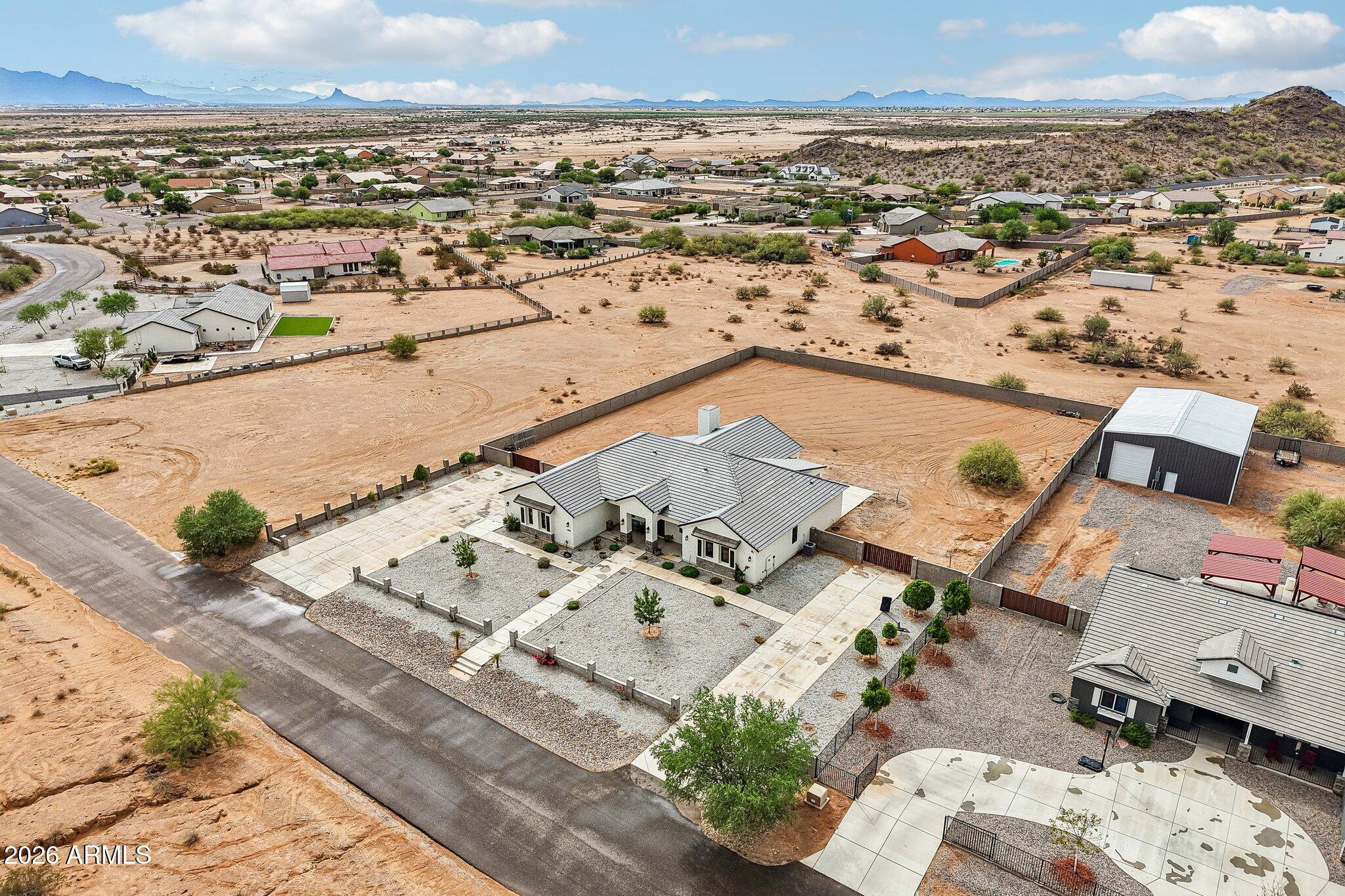 Aerial view of a desert home with a fenced yard, detached metal outbuilding, and distant mountains.
