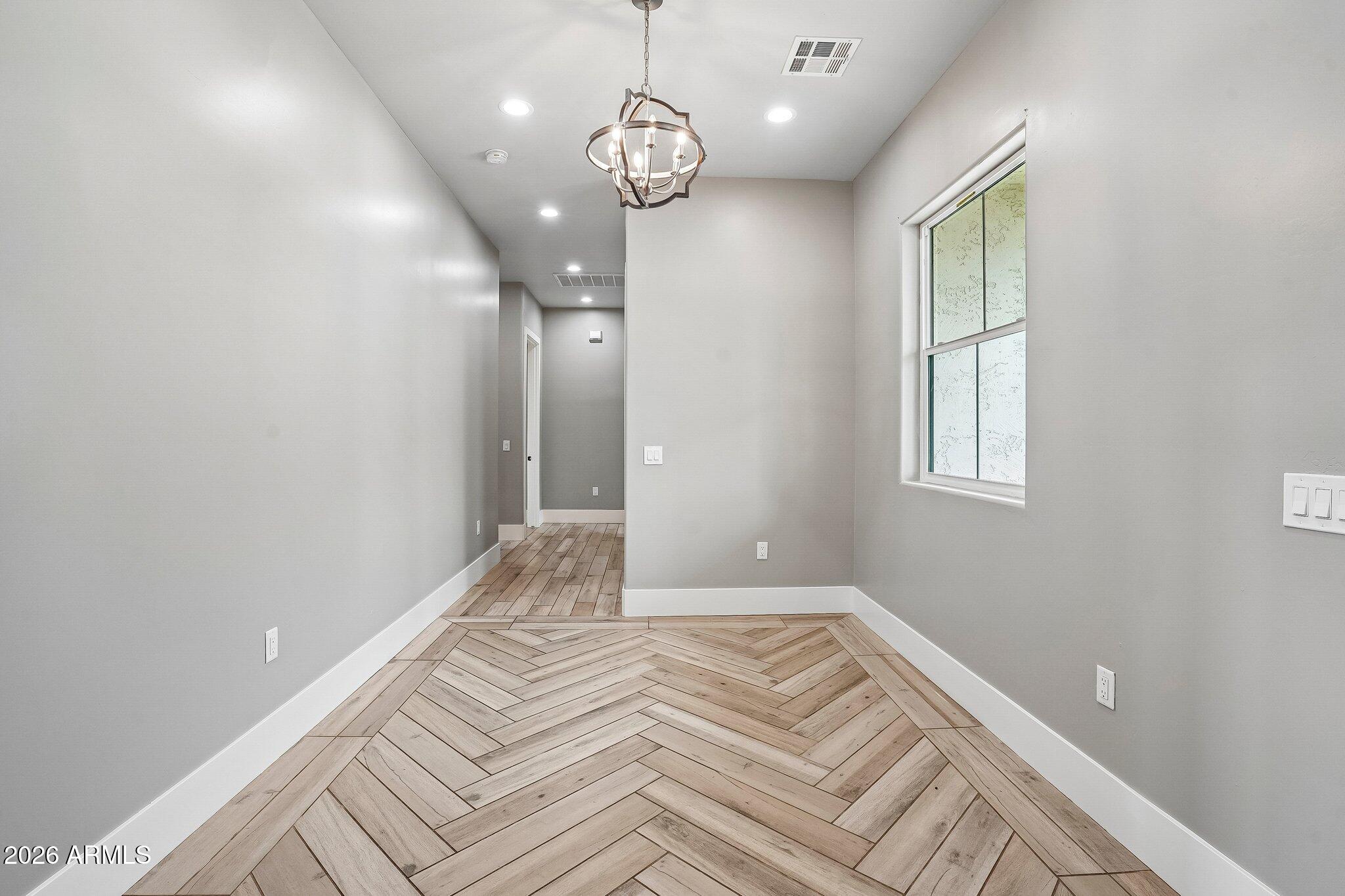 Empty dining area with herringbone wood flooring, a hanging chandelier, and a textured-glass window.