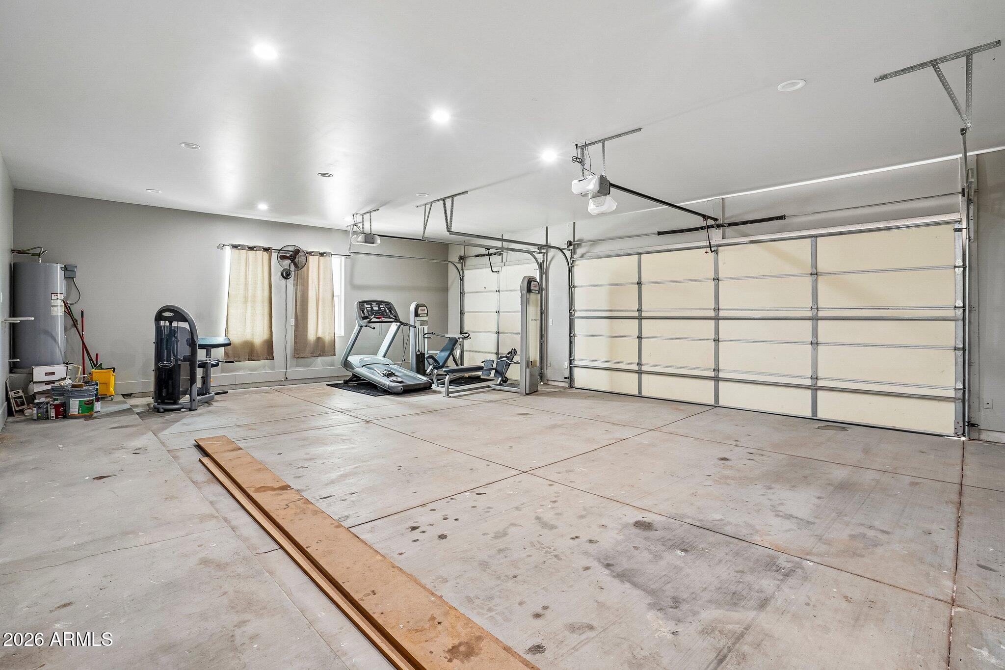 Garage gym with a treadmill and weight machines beside a wide sectional garage door.