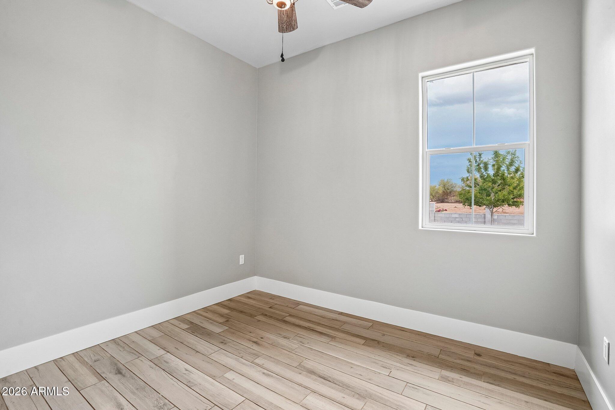 Empty room with wood-look plank flooring, a ceiling fan, and a window overlooking a tree.