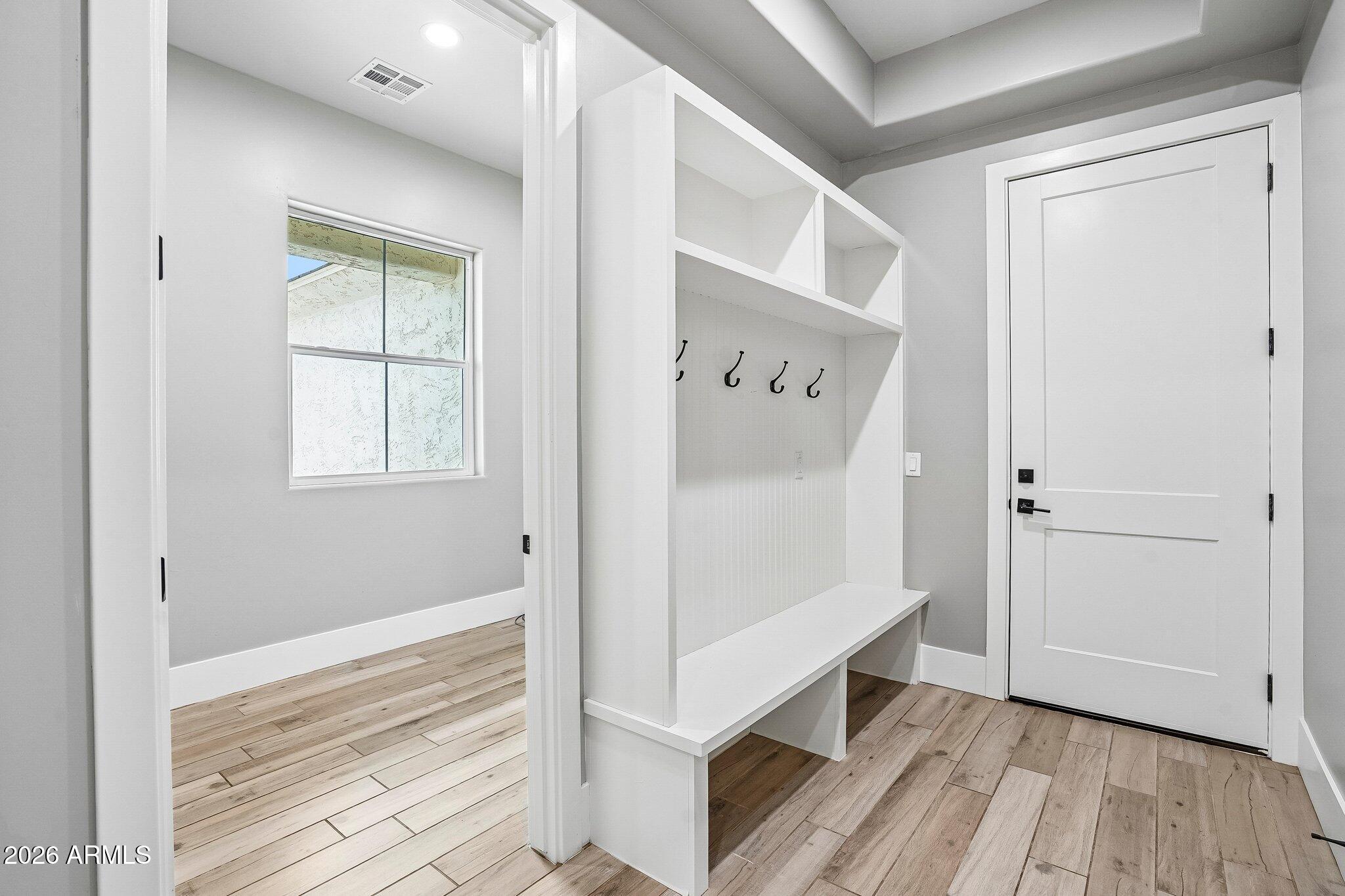 Entryway with a white built-in bench, coat hooks, cubbies, and wood-look flooring.