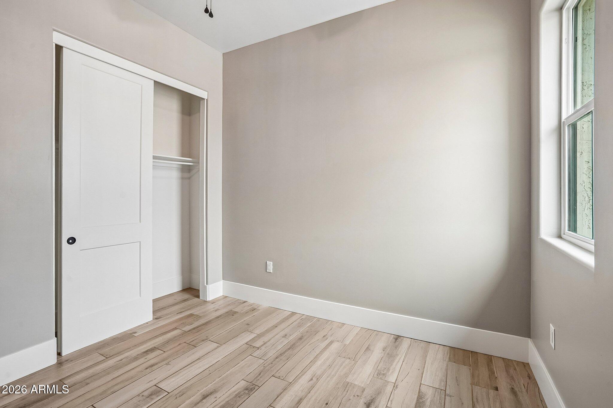 Empty room with wood-look plank flooring, a window, and an open sliding-door closet.