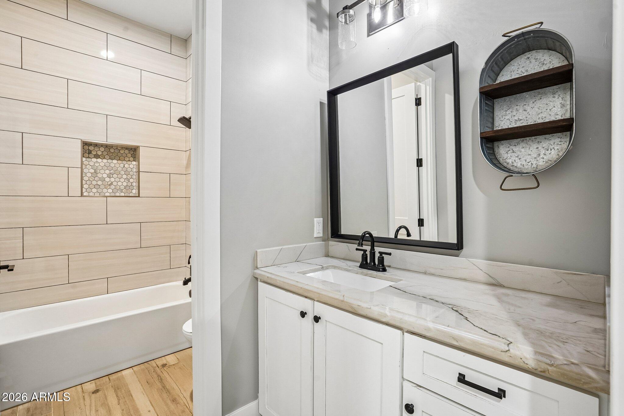 Bathroom vanity with a veined stone countertop beside a bathtub with light wood-look tile walls.
