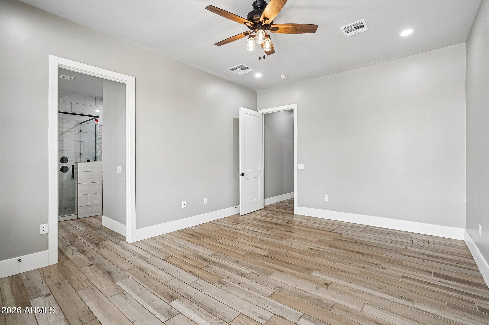 Empty bedroom with wood-look tile flooring, a ceiling fan, and an adjoining tiled bathroom.
